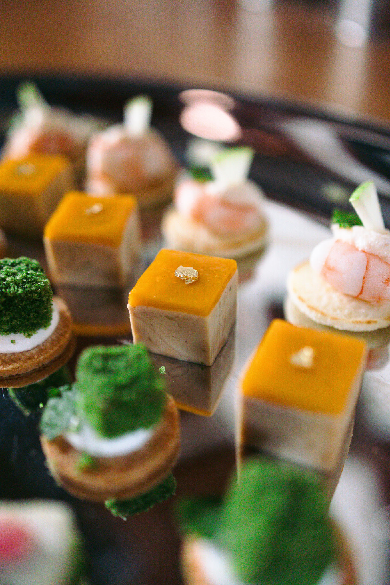Close-up of French wedding canapes including foie gras with gold leaf and prawn tartlets on dark tray