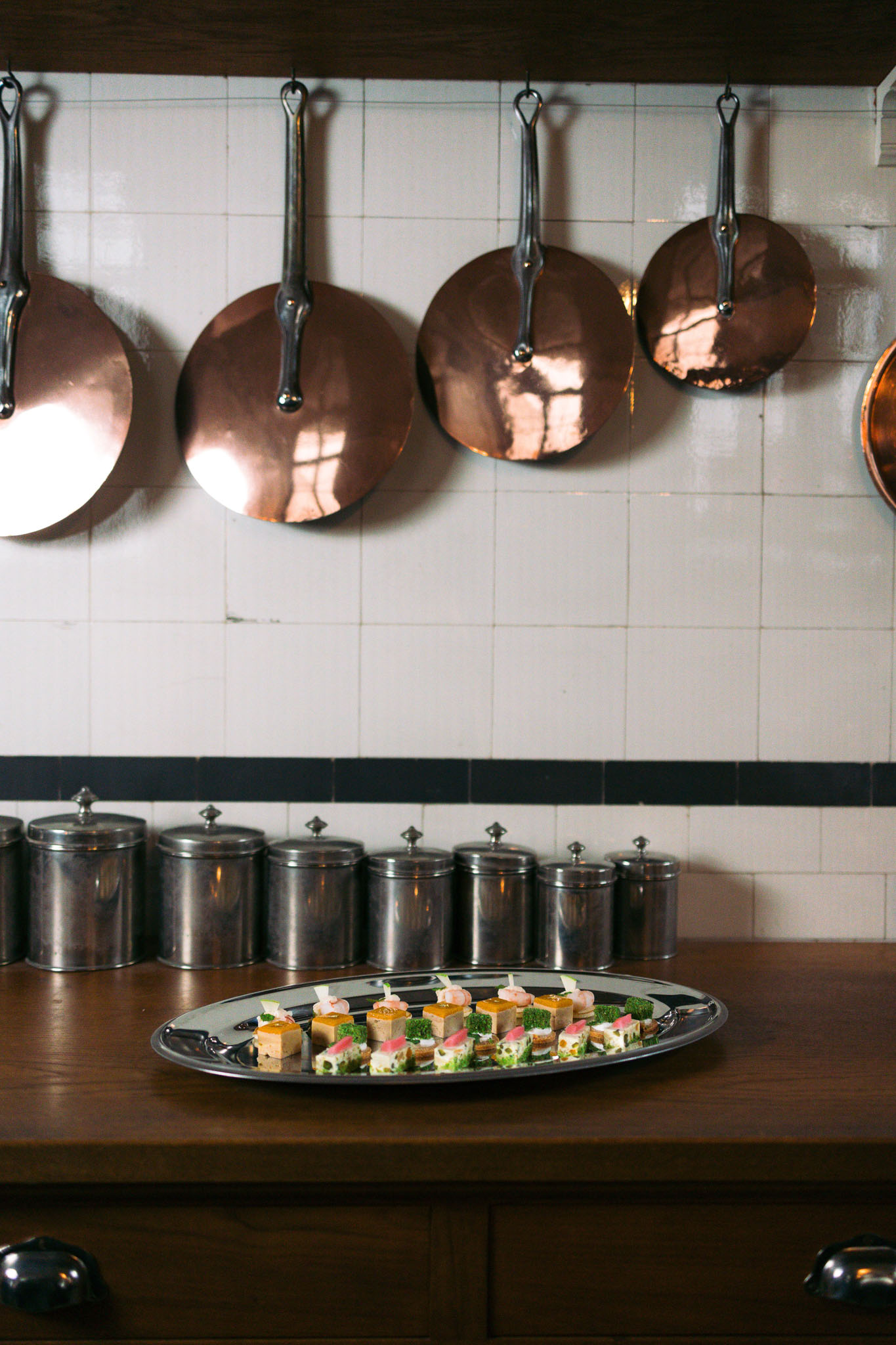 Silver tray of canapes with foie gras shrimp and herbs below copper pans in chateau kitchen