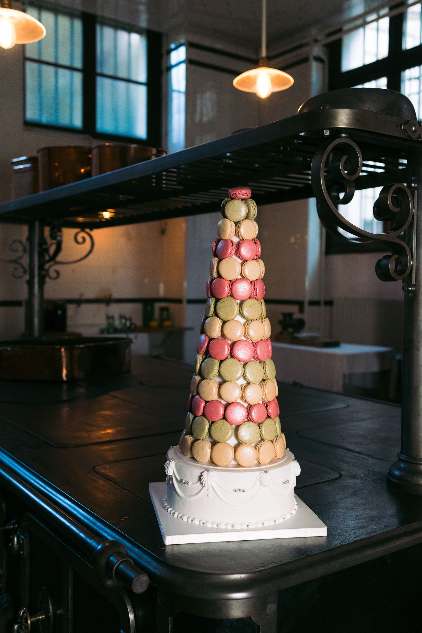 Macaron tower in pink, sage, peach, and champagne on pearl-detailed base in industrial venue