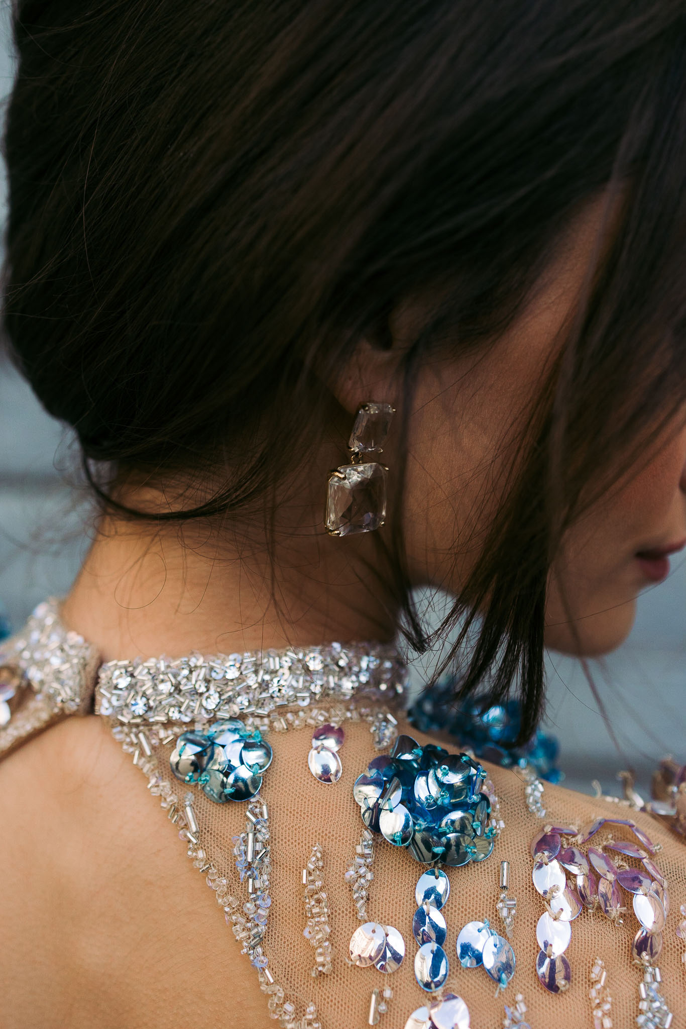 Close-up of crystal drop earring and beaded dress with blue and lavender sequin appliques on woman from behind