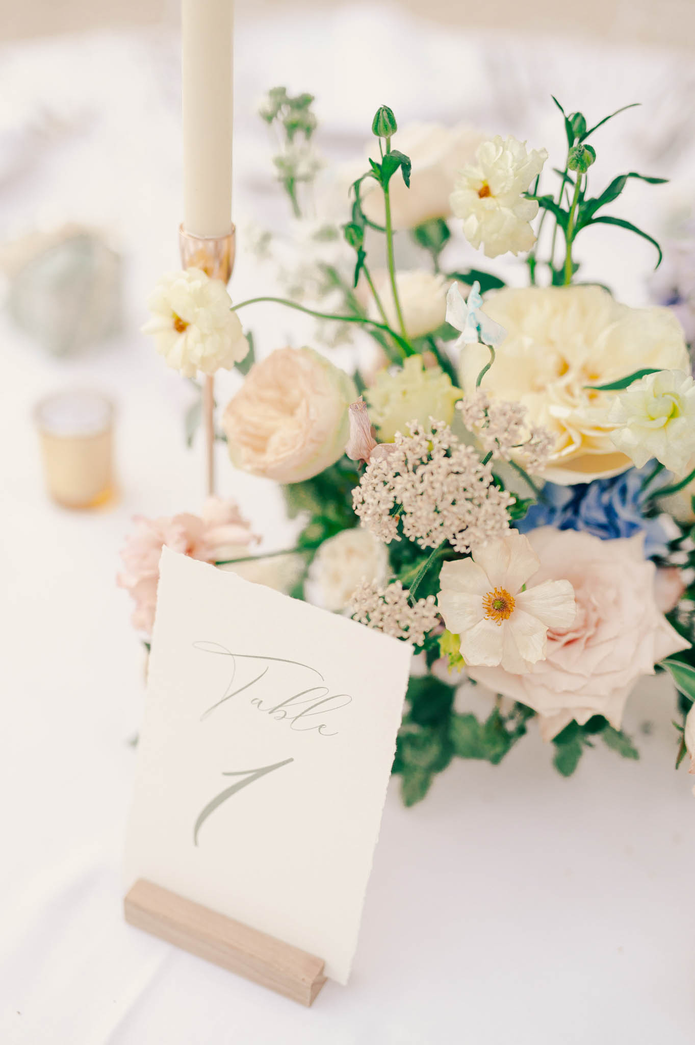 Table number card reading Table 1 with pastel centerpiece of blush roses, cream peonies, blue hydrangea, and gold candlestick