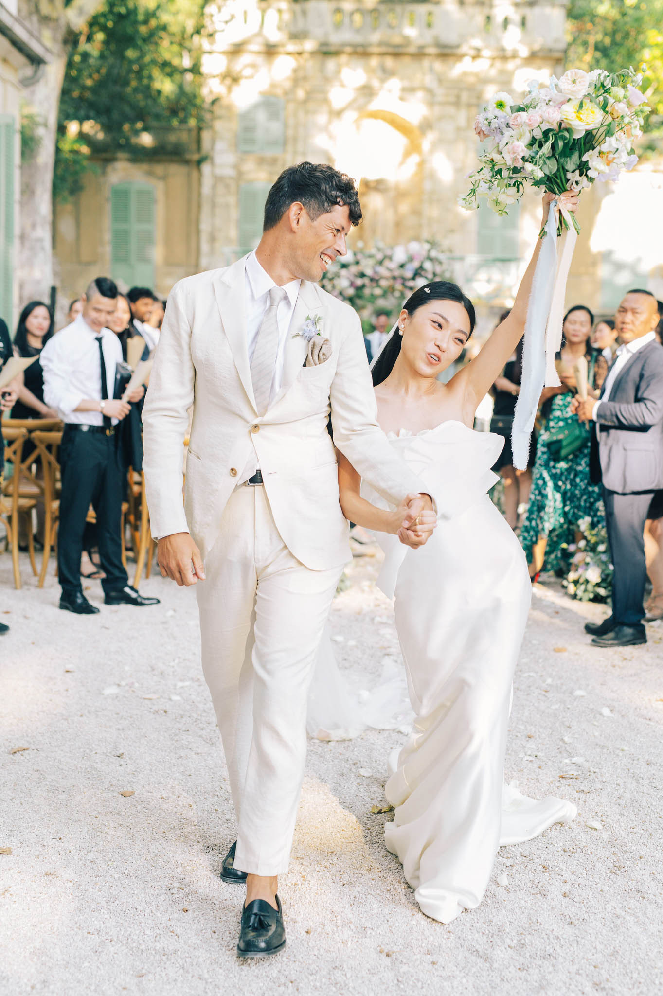Bride and groom laughing as they walk back up the aisle after outdoor ceremony at a French chateau courtyard