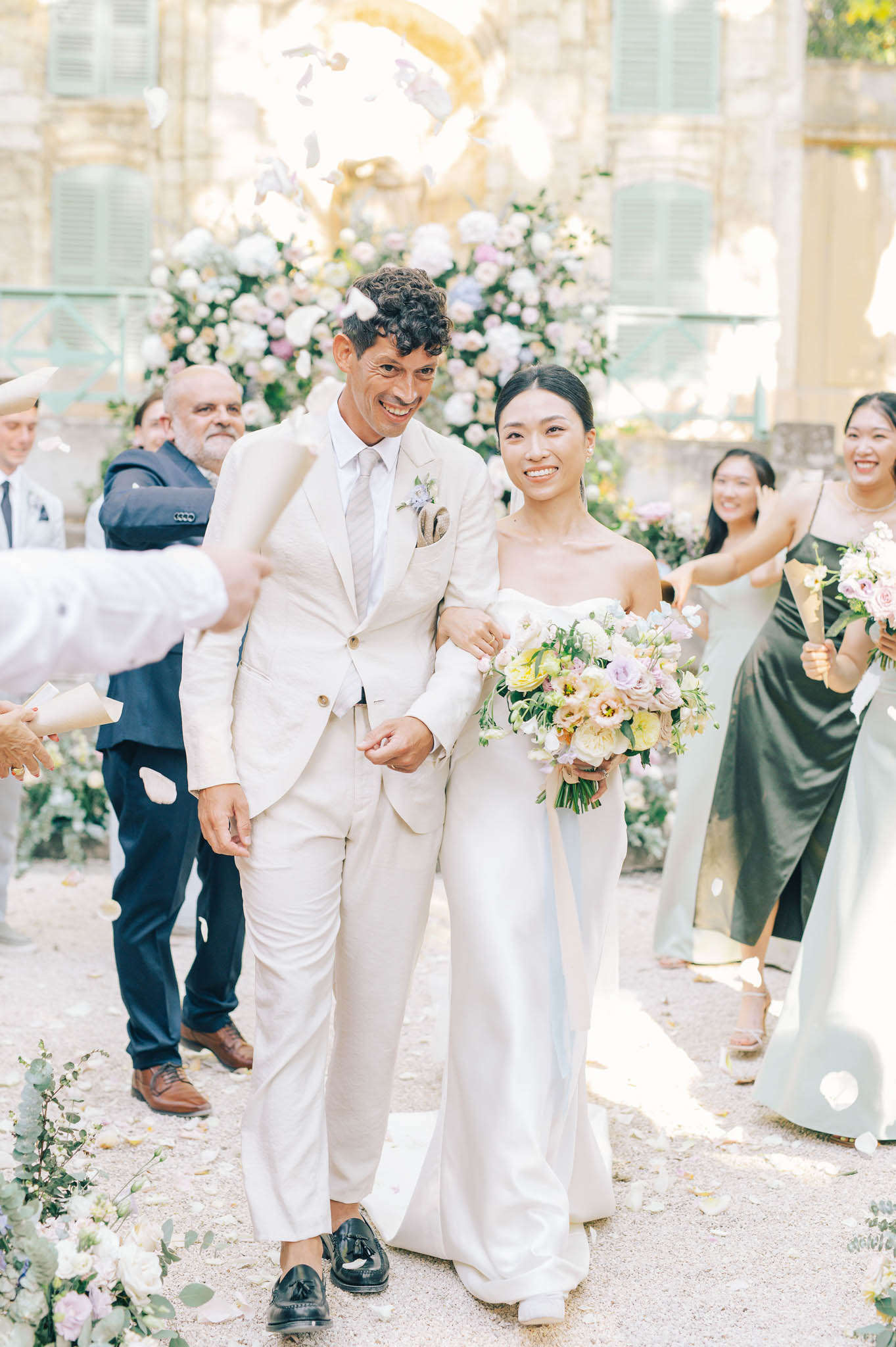 Couple walking up aisle during petal toss with circular floral backdrop and green bridesmaids