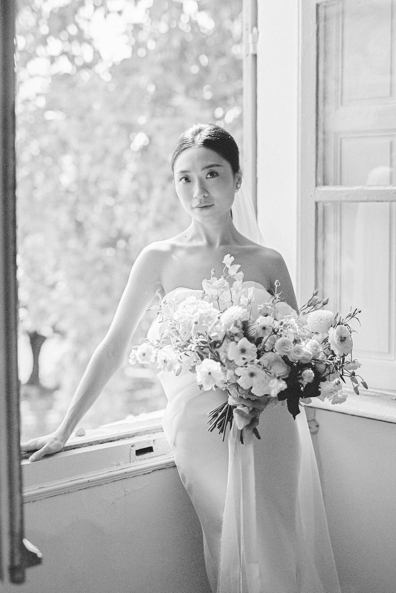 Black and white bride at open French window holding lush bouquet with ribbon streamers and long veil