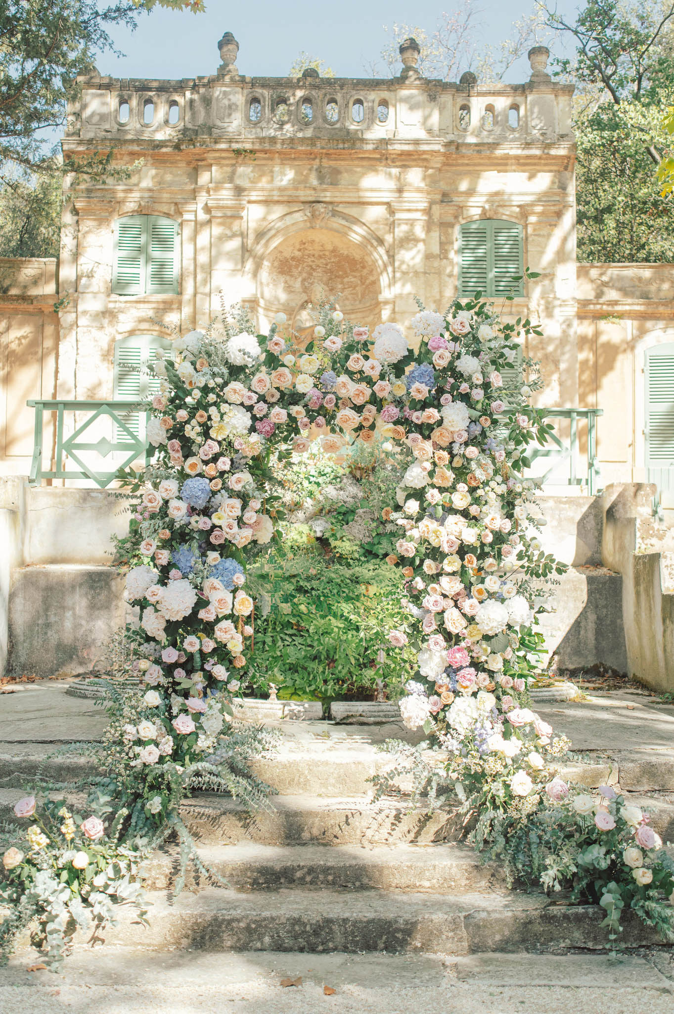 Floral arch with blush roses, blue hydrangeas, and peach blooms at chateau entrance steps