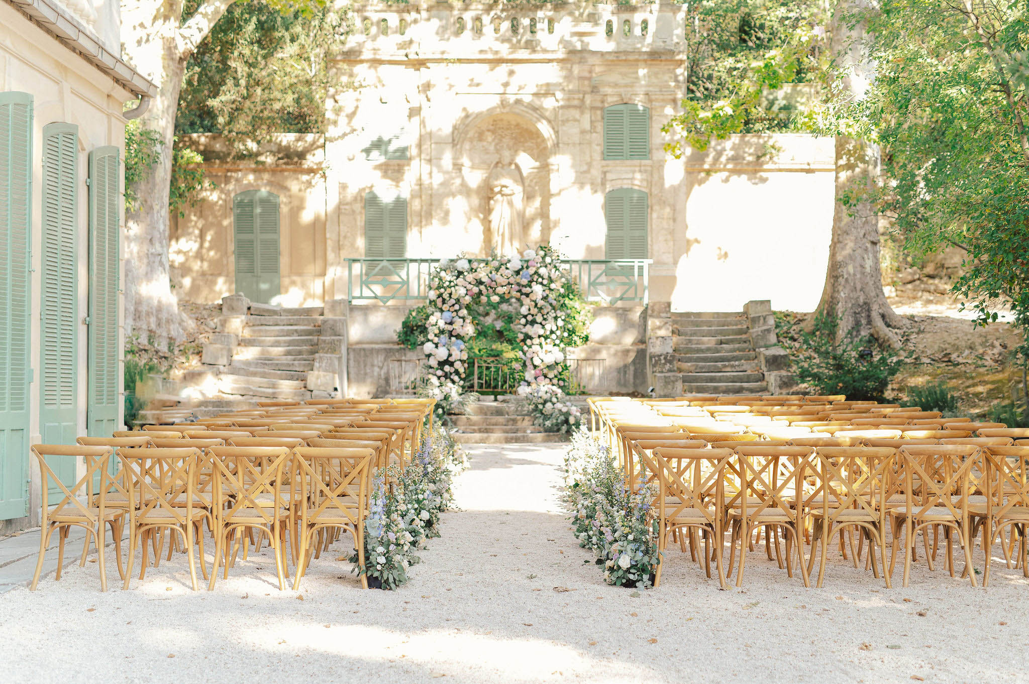 Outdoor wedding ceremony setup with cross-back chairs and floral arch in French chateau courtyard