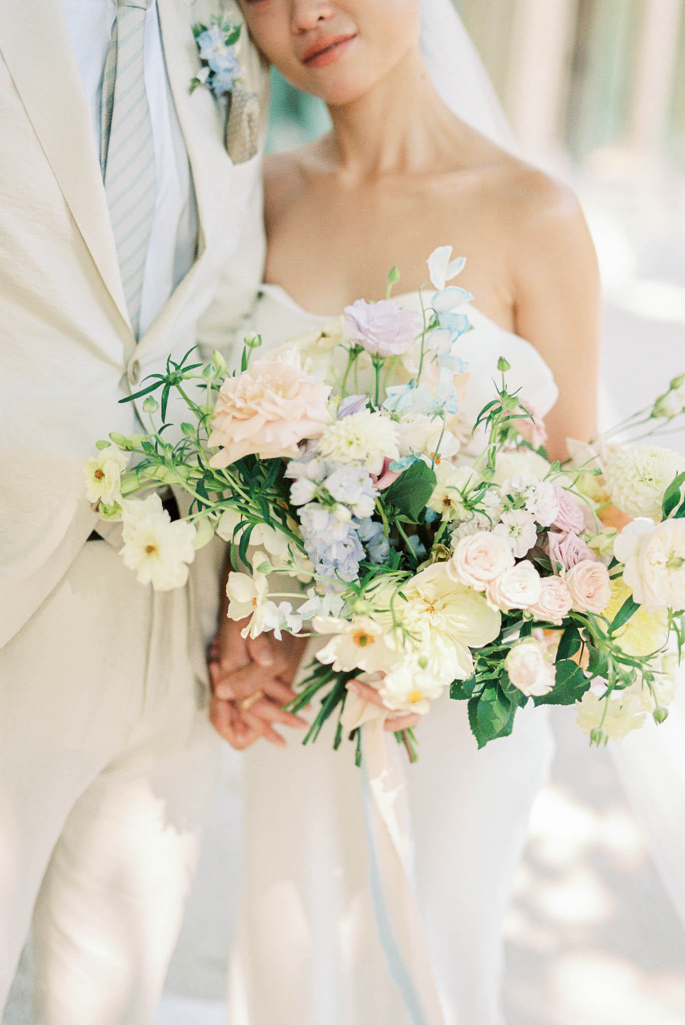 Pastel bouquet of blush roses, lavender lisianthus, and blue delphinium with trailing ribbon close-up