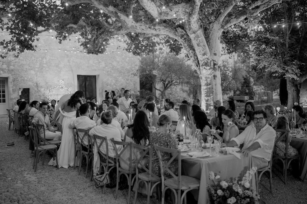 Black and white courtyard dinner under plane trees with fairy lights and cross-back chairs
