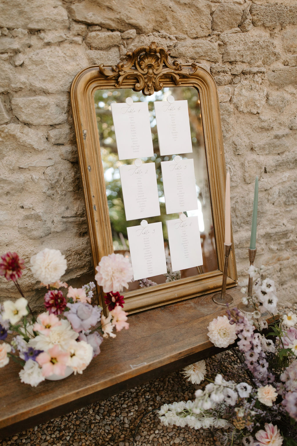 Gold-framed mirror seating chart with calligraphy table cards, blush dahlias, burgundy blooms, and brass candlesticks
