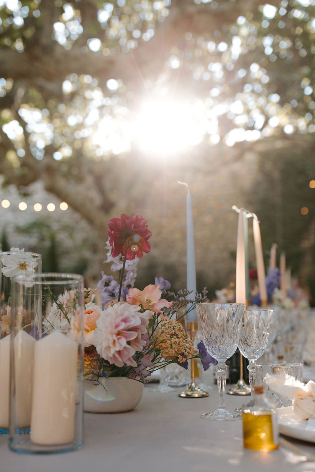 Outdoor reception table with blush and pink dahlia centerpiece, crystal stemware, and pastel taper candles