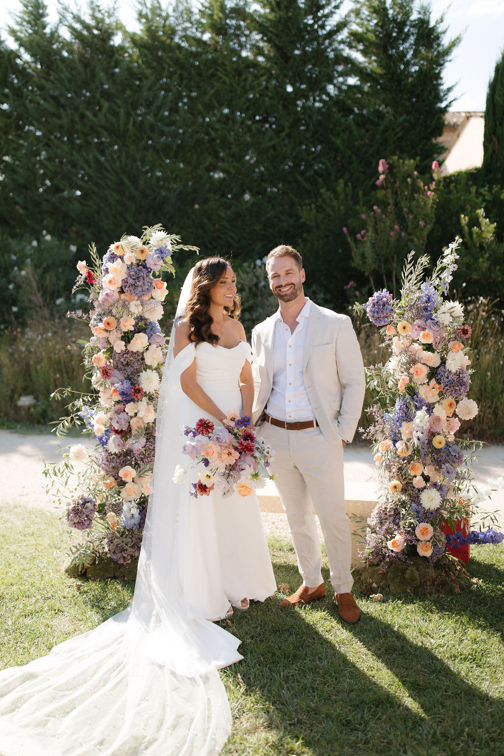 Couple between two tall floral columns of purple hydrangea, peach roses, and burgundy cosmos