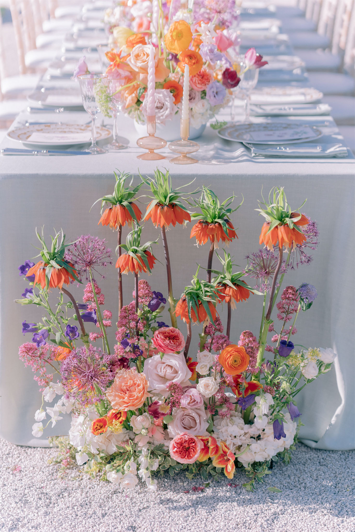 Maximalist tablescape with orange fritillaria purple alliums blush roses on powder blue linen with gold-rimmed china