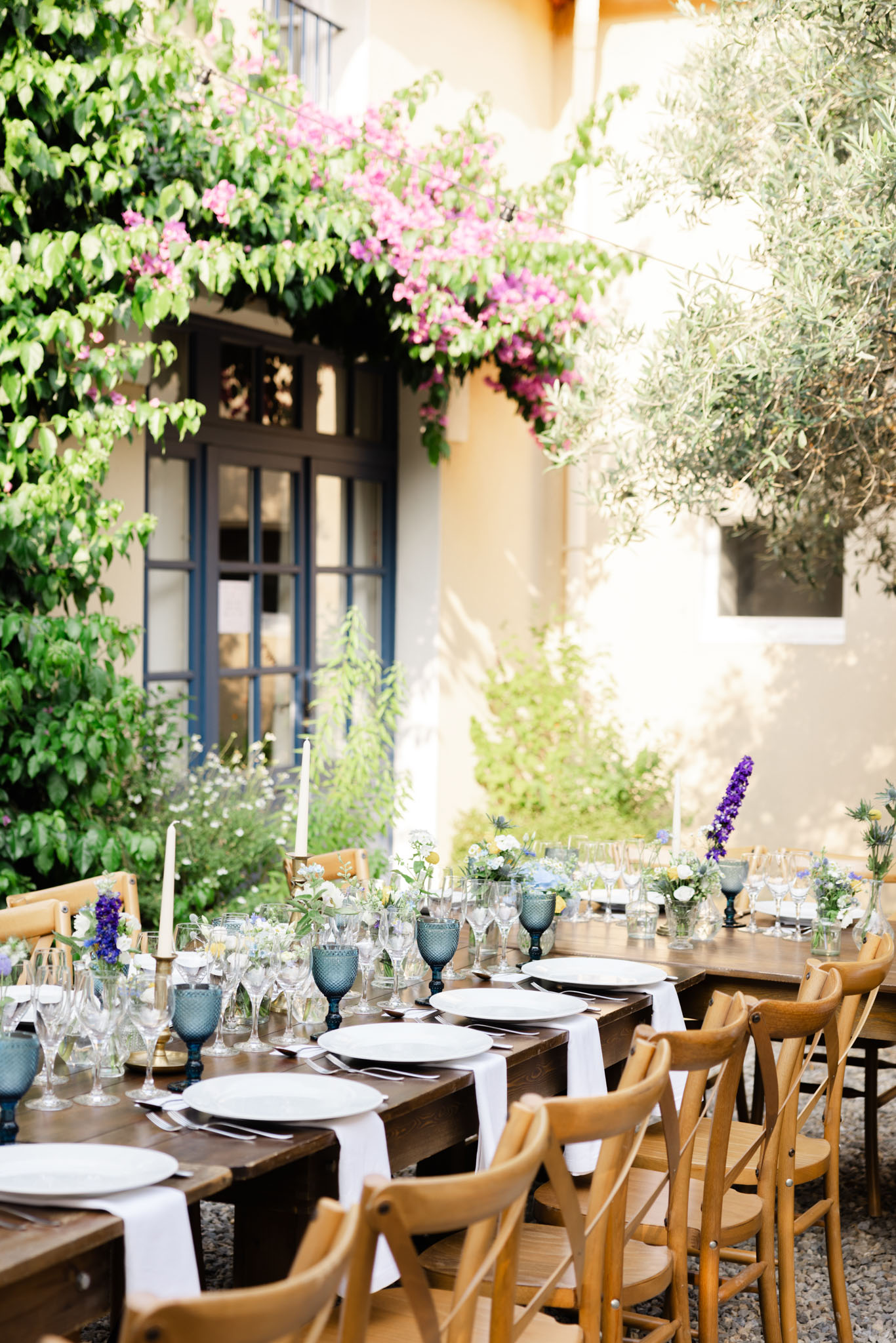 Rustic reception table with blue goblets, wildflower centerpieces, and taper candles before bougainvillea facade