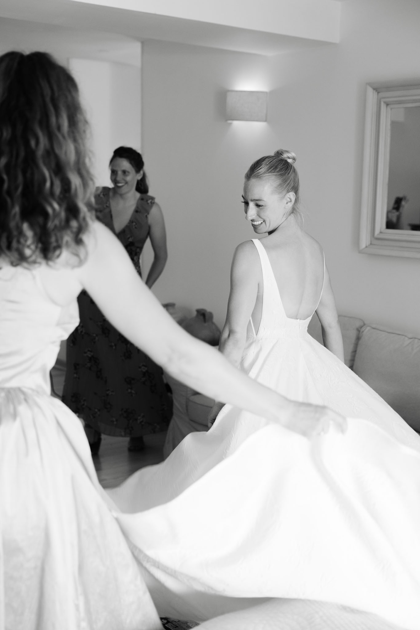 Bride swirls ballgown skirt with help of friend in hotel room during joyful getting-ready moment in B&W