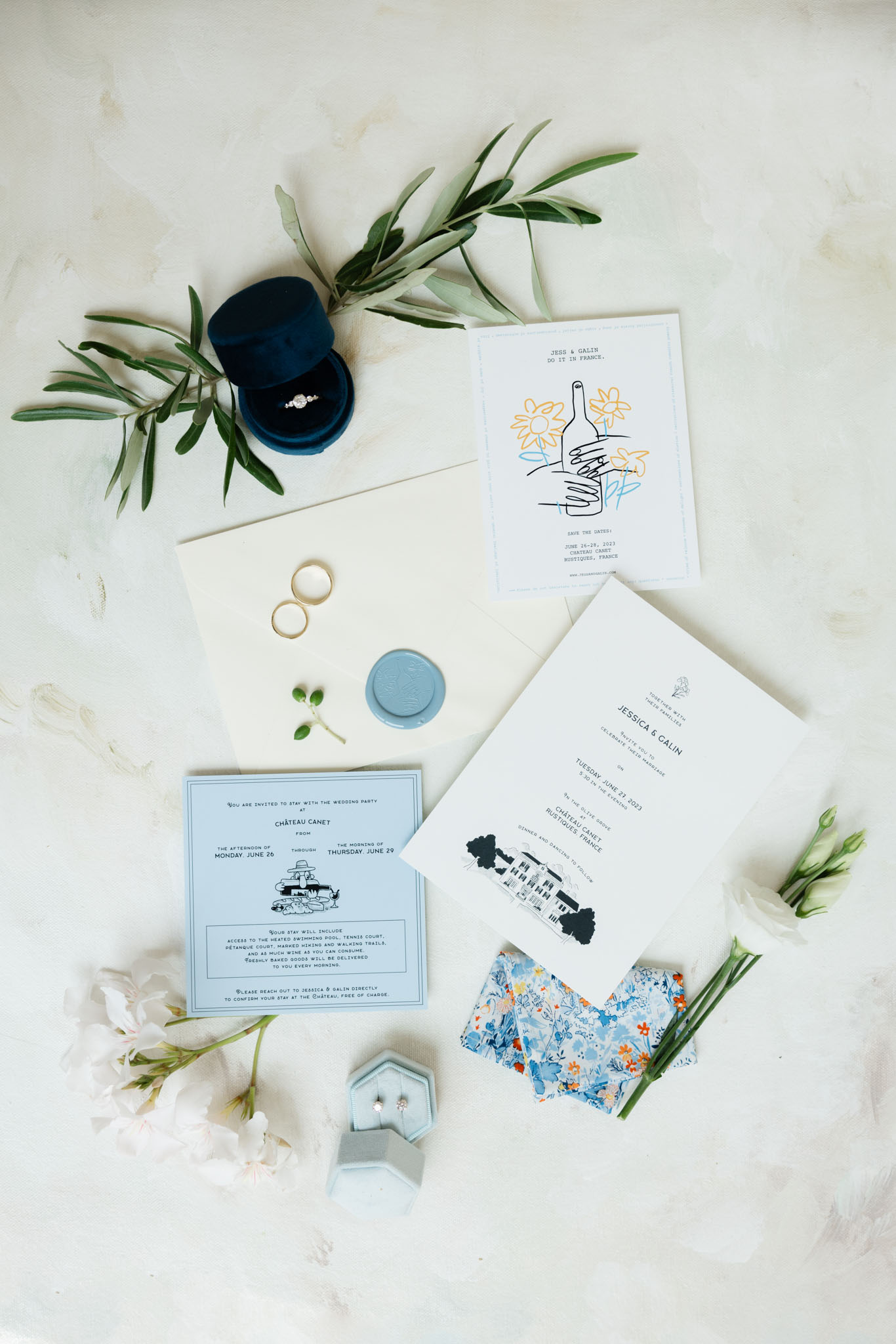 Blue and cream stationery suite with chateau illustration, navy velvet ring box, and olive leaf sprigs