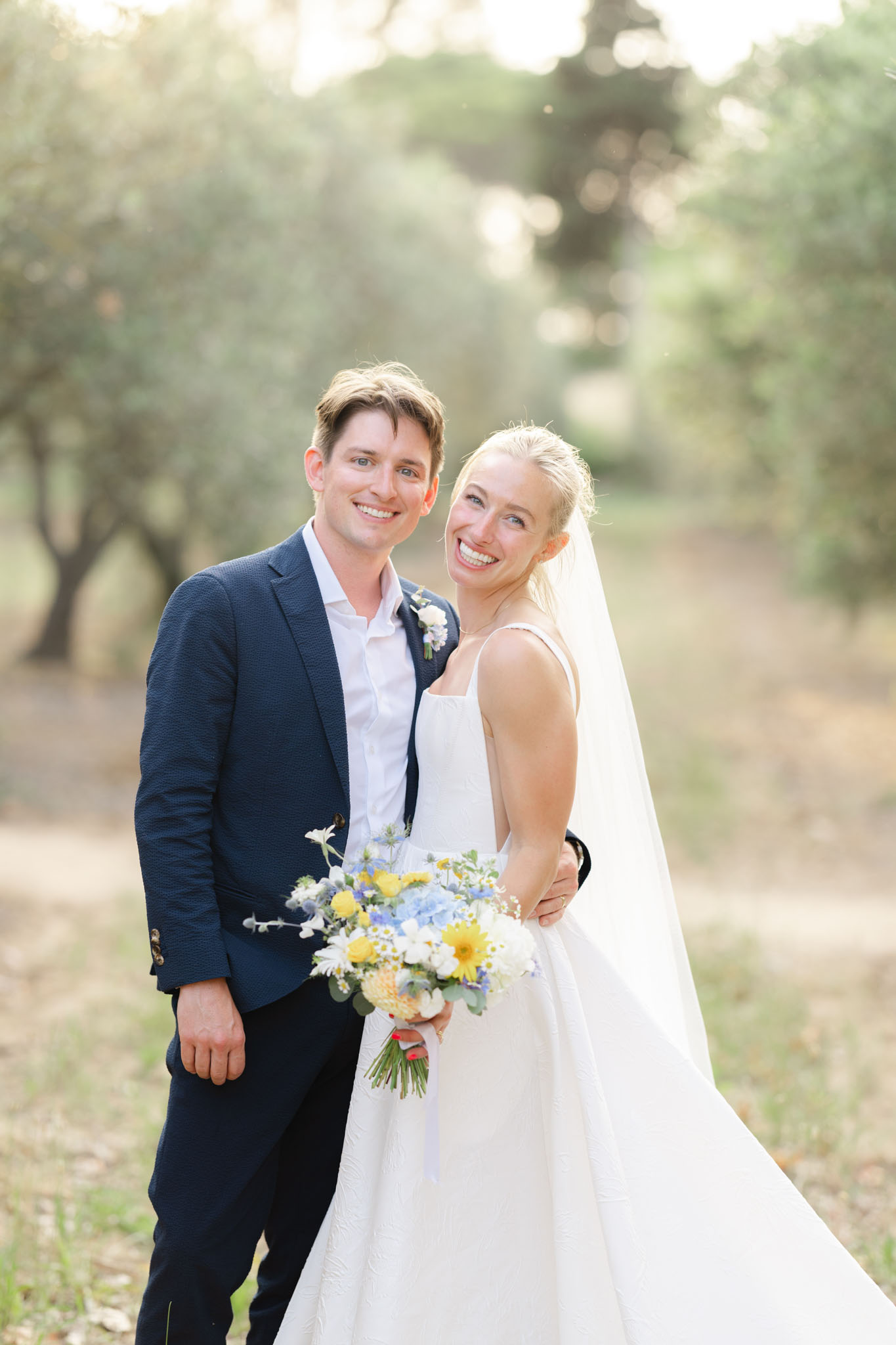 Bride with yellow gerbera and blue hydrangea bouquet and groom in navy blazer in olive grove