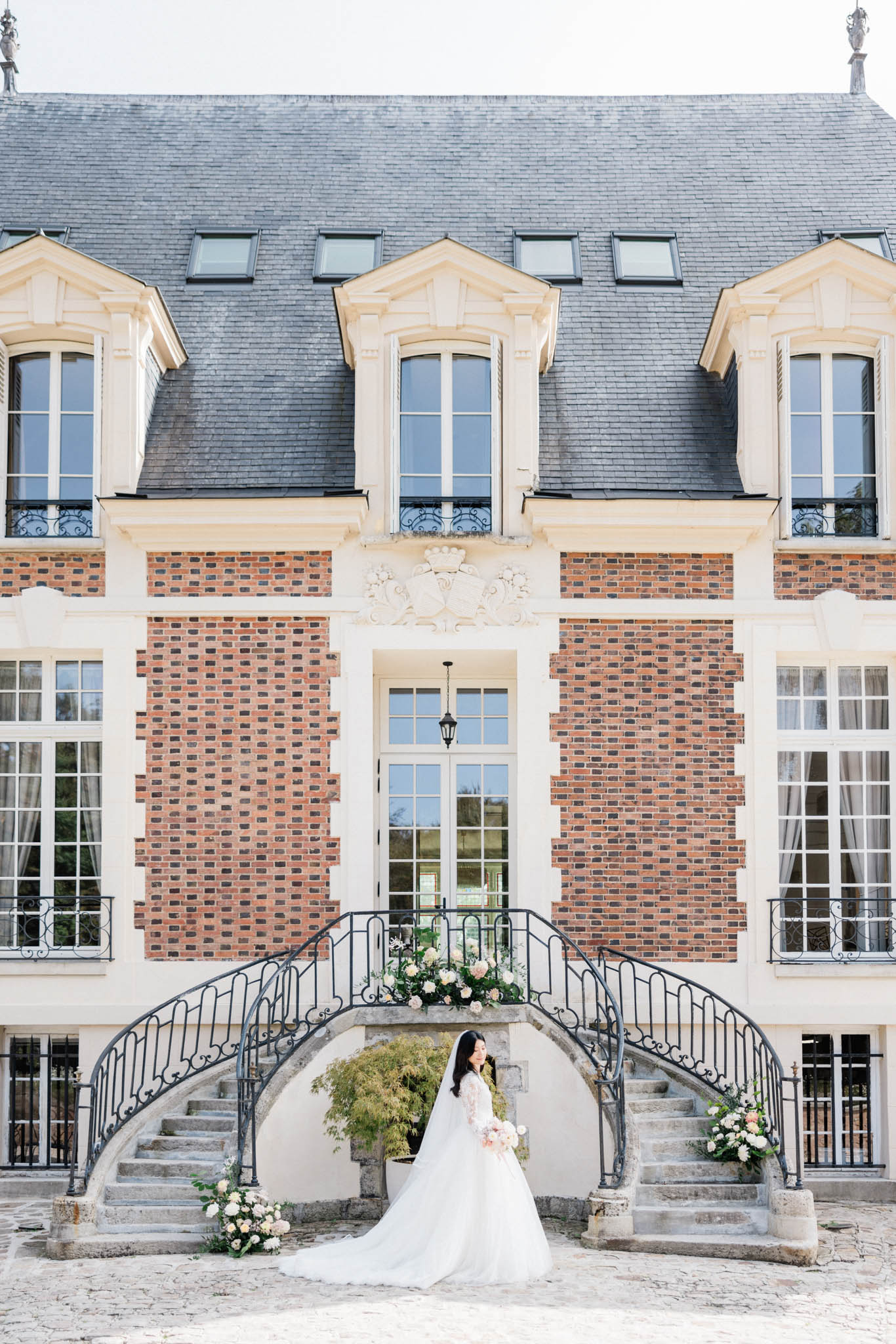 Bride in long-sleeve ball gown with cathedral train at base of chateau wrought-iron double staircase