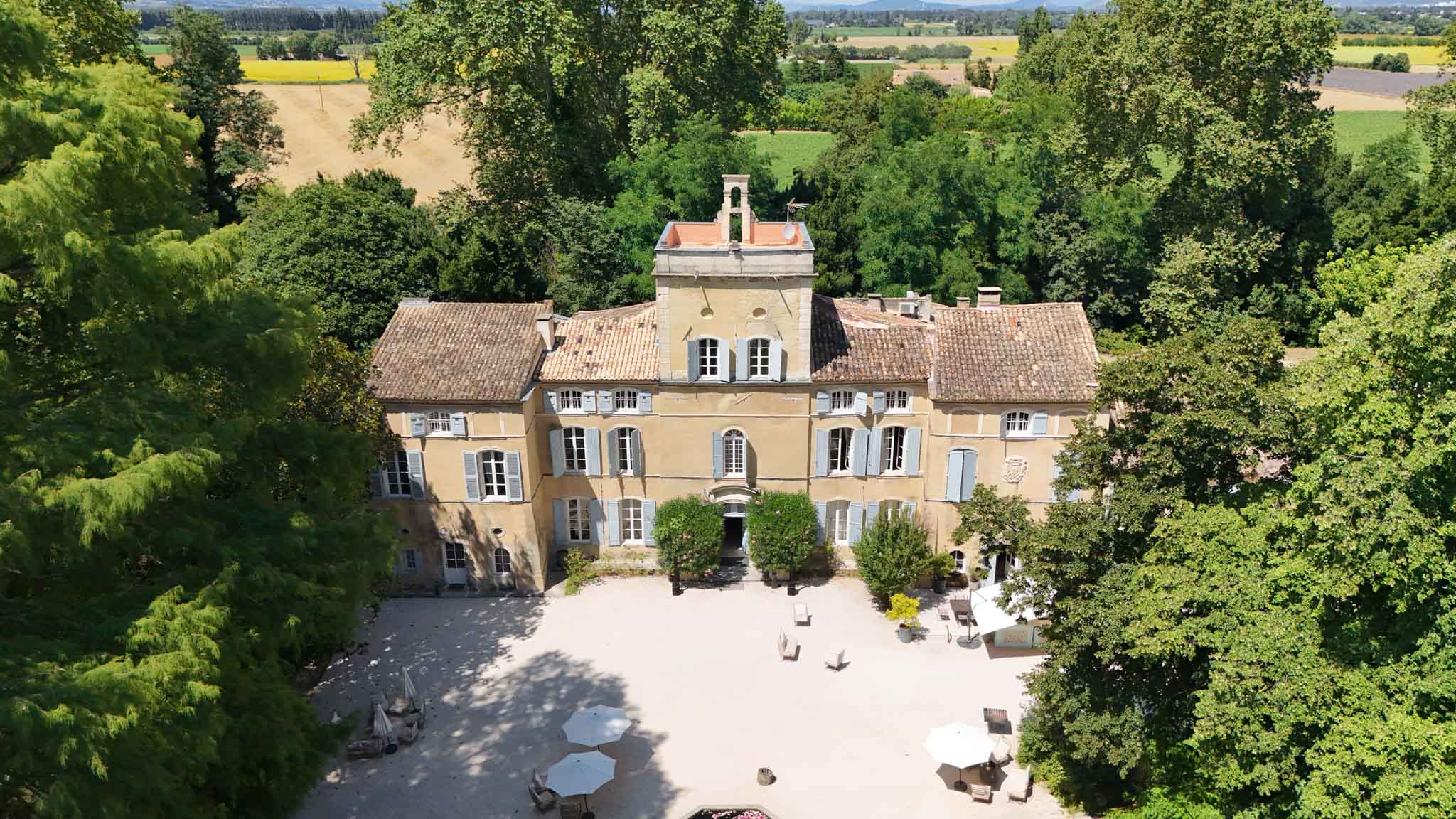 Aerial drone view of Provencal chateau with honey-yellow walls, gravel courtyard, and lavender fields beyond