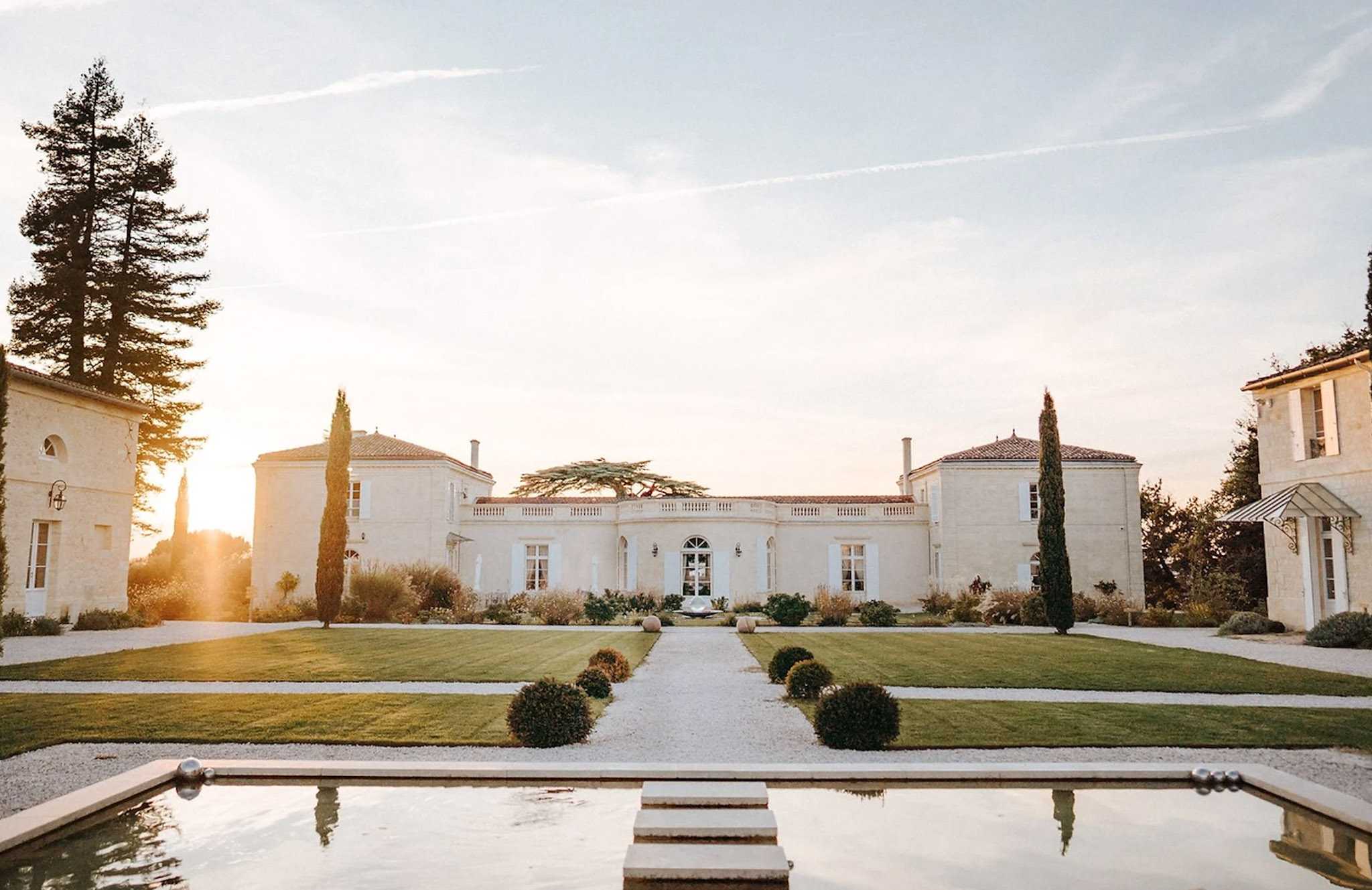French chateau exterior at golden hour with reflecting pool, gravel path, and boxwood topiaries
