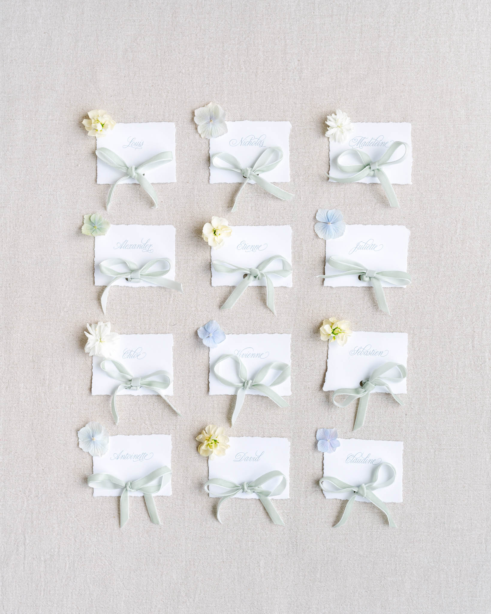 Grid of twelve deckle-edged place cards with calligraphy sage ribbon bows and dried flower accents