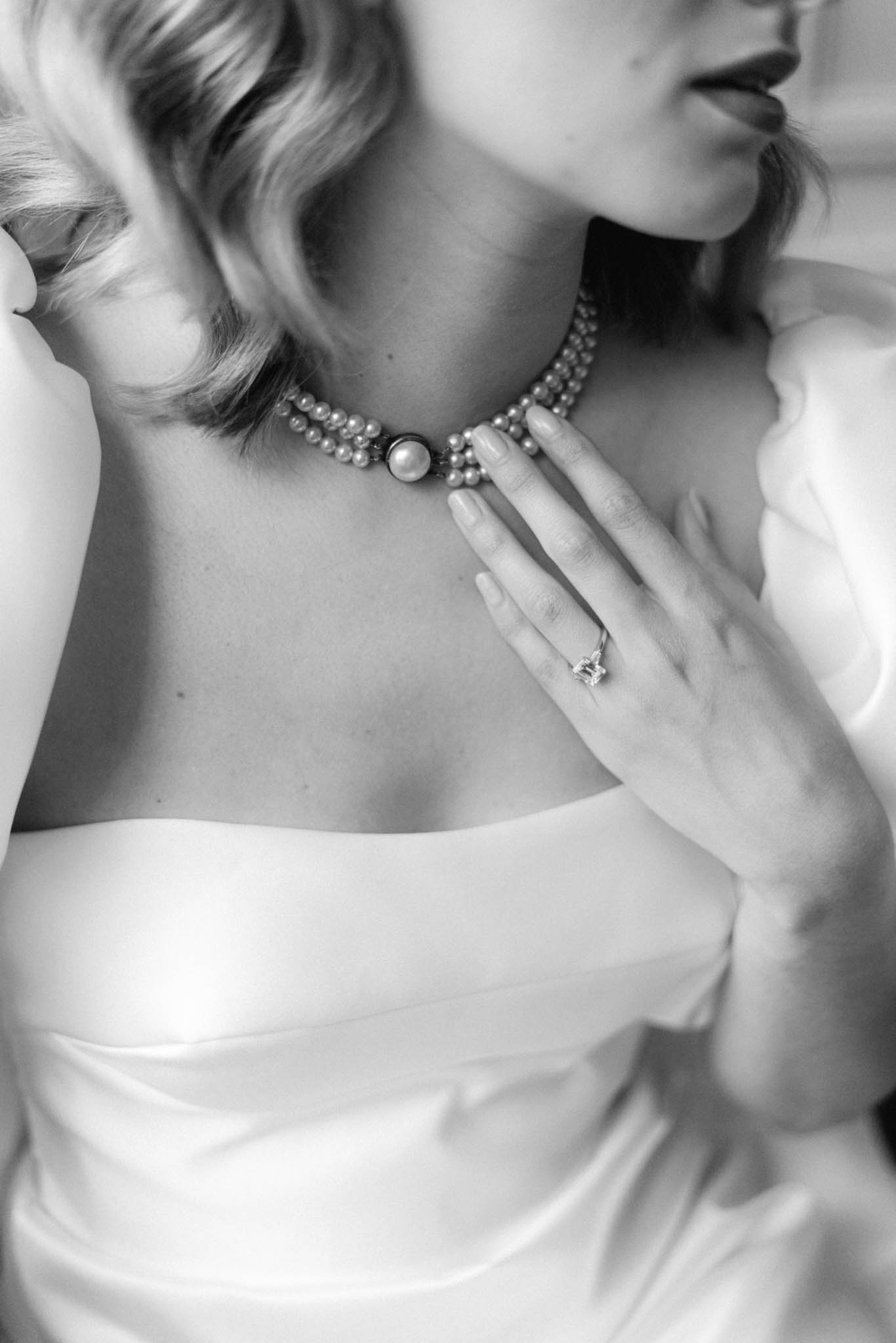 Black-and-white close-up of bride in strapless satin gown with pearl choker and diamond engagement ring