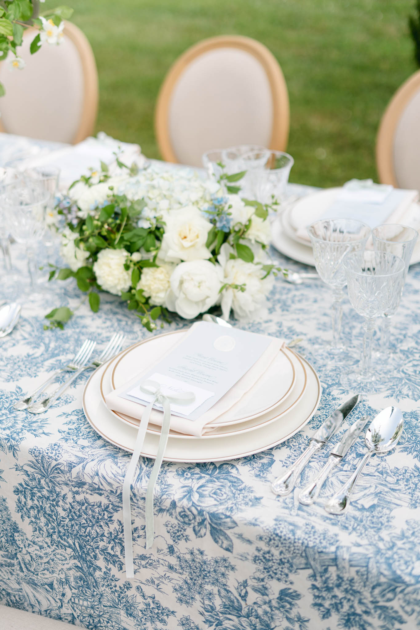 Blue toile tablecloth place setting with ivory roses blue delphinium gold-rimmed plates and crystal glasses