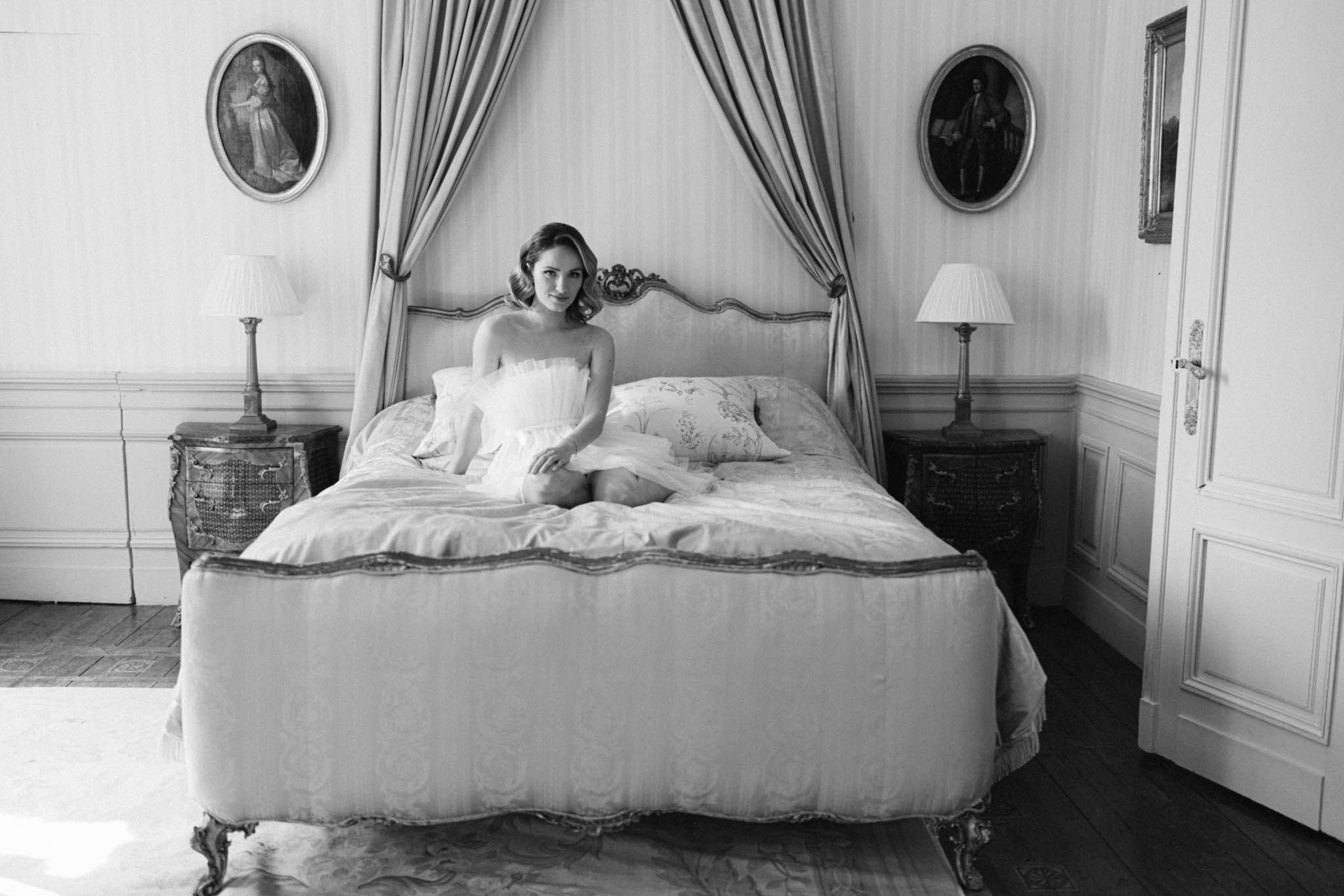 Black and white bride in strapless robe on ornate bed in chateau bedroom with Louis XVI headboard and oval portrait paintings