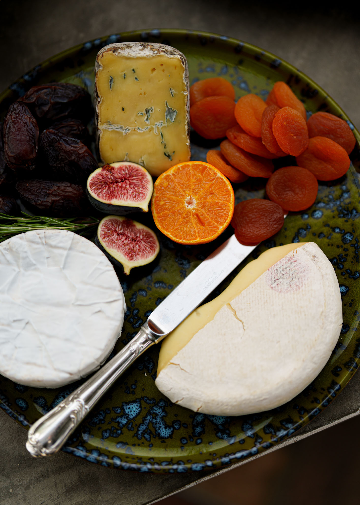 French cheese board with camembert, blue cheese, fresh figs, dried fruit, and rosemary on ceramic plate