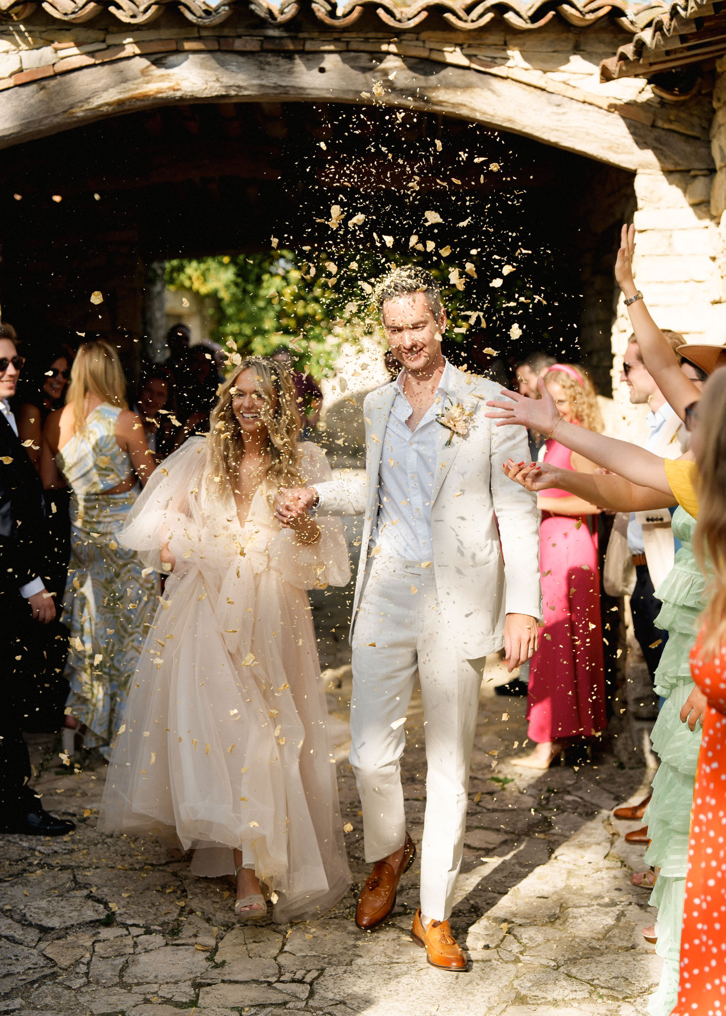 Couple walking through gold confetti exit under stone archway with bride in blush tulle gown