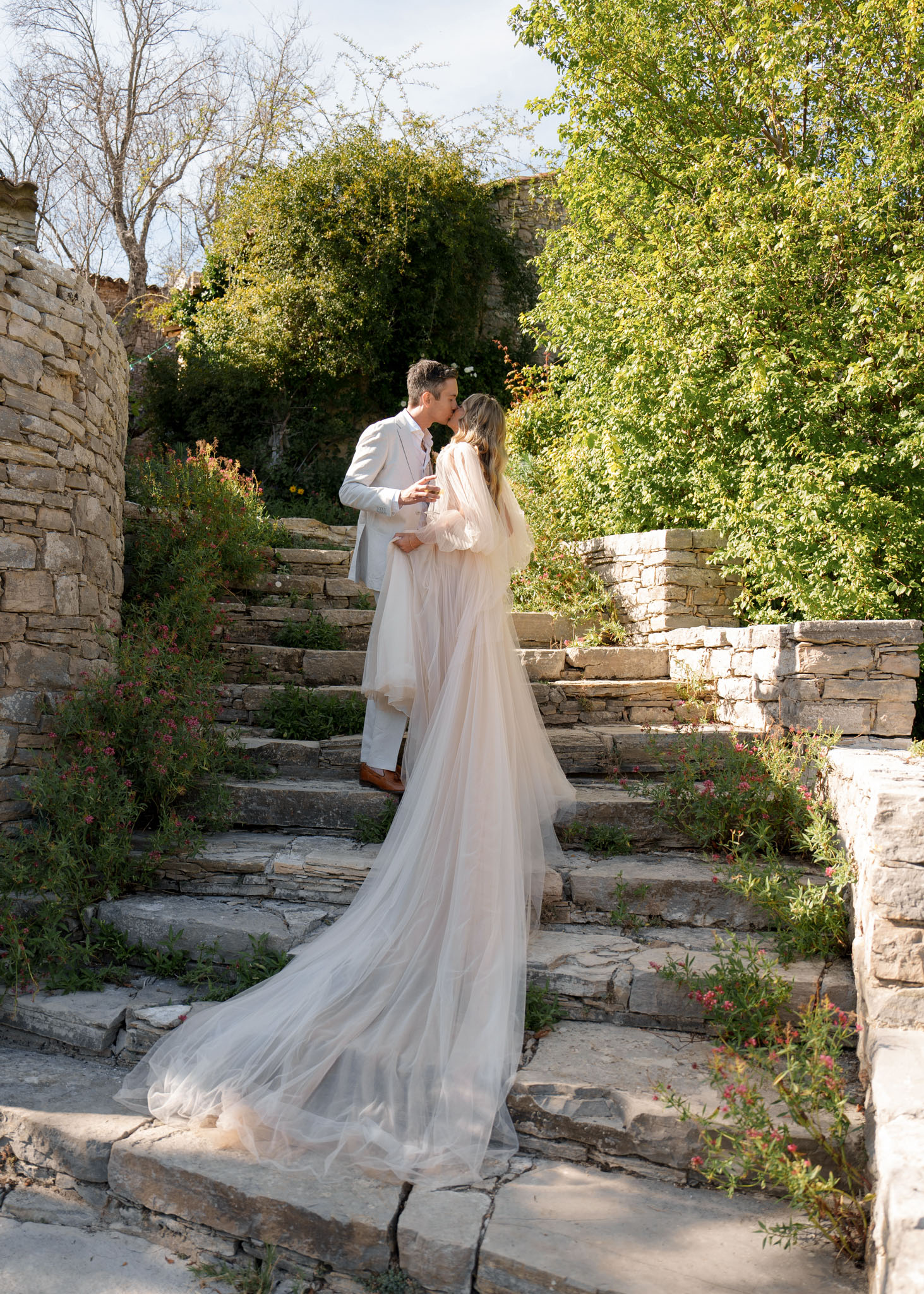 Couple kissing on stone staircase with bride's cathedral-length tulle train cascading down the steps