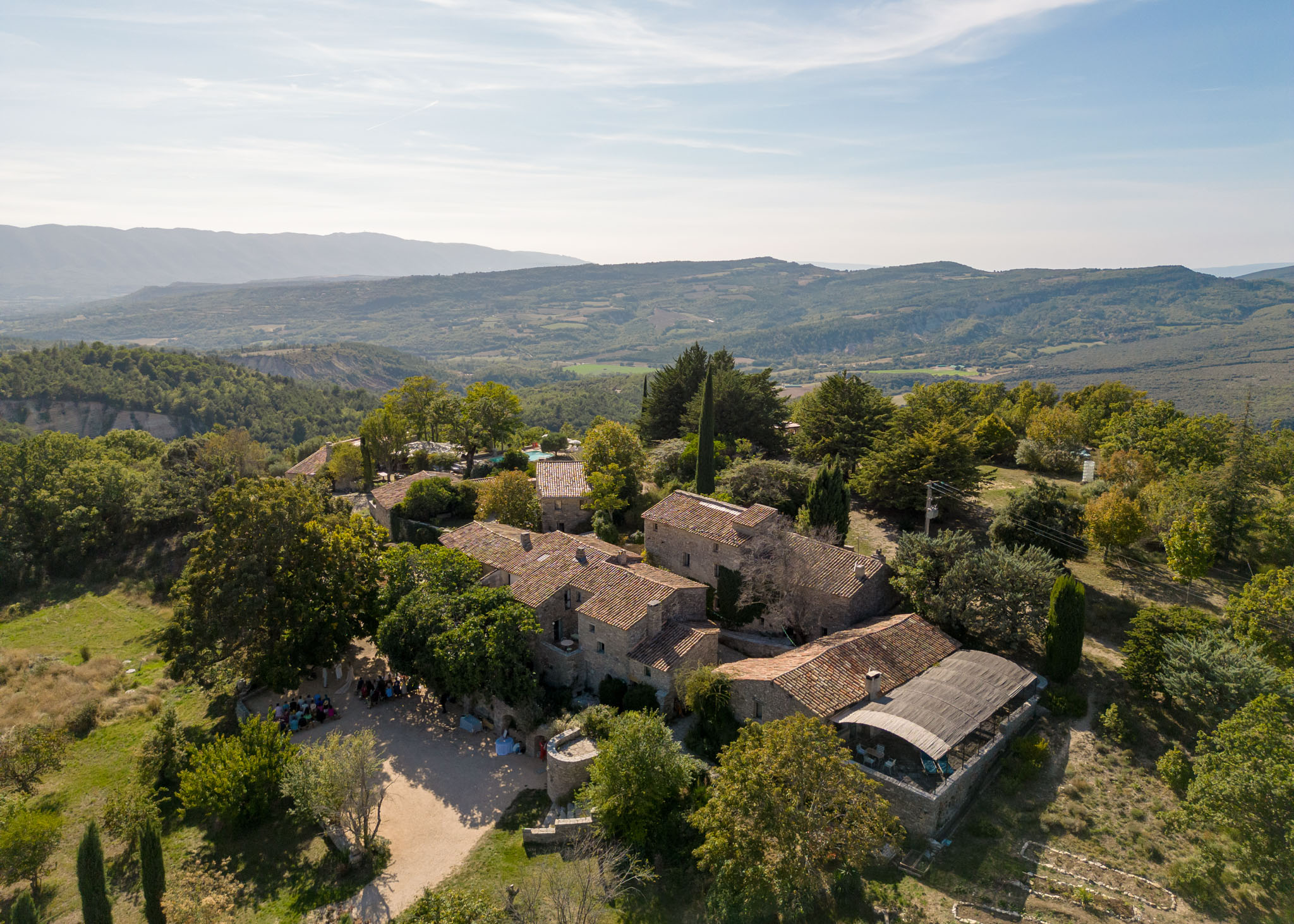 Aerial drone view of a Provencal stone mas estate with wedding guests gathered in the courtyard
