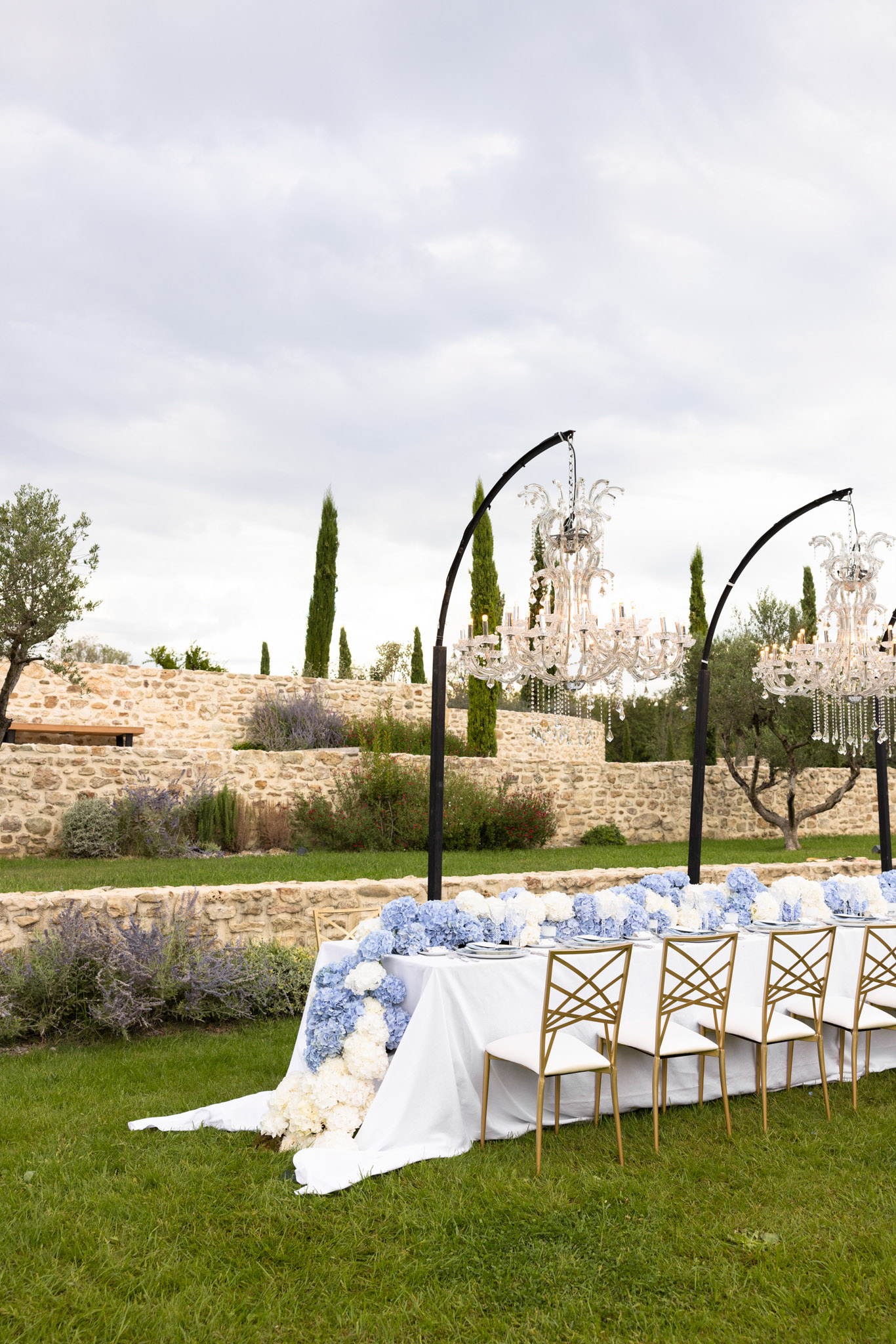 Garden reception with blue hydrangea cascade crystal chandeliers on arc stands gold cross-back chairs and lavender border