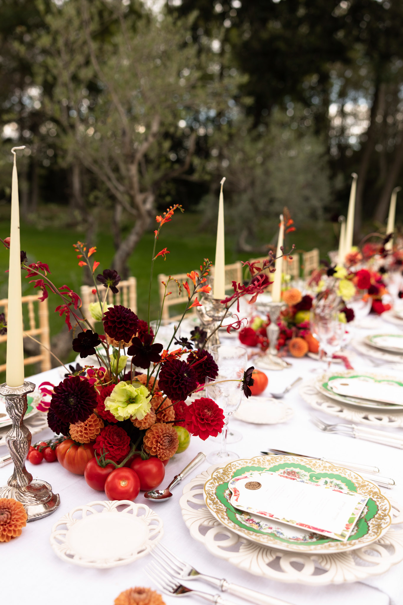 Autumnal reception tablescape with burgundy dahlias, heirloom tomatoes, silver candlesticks, and vintage china
