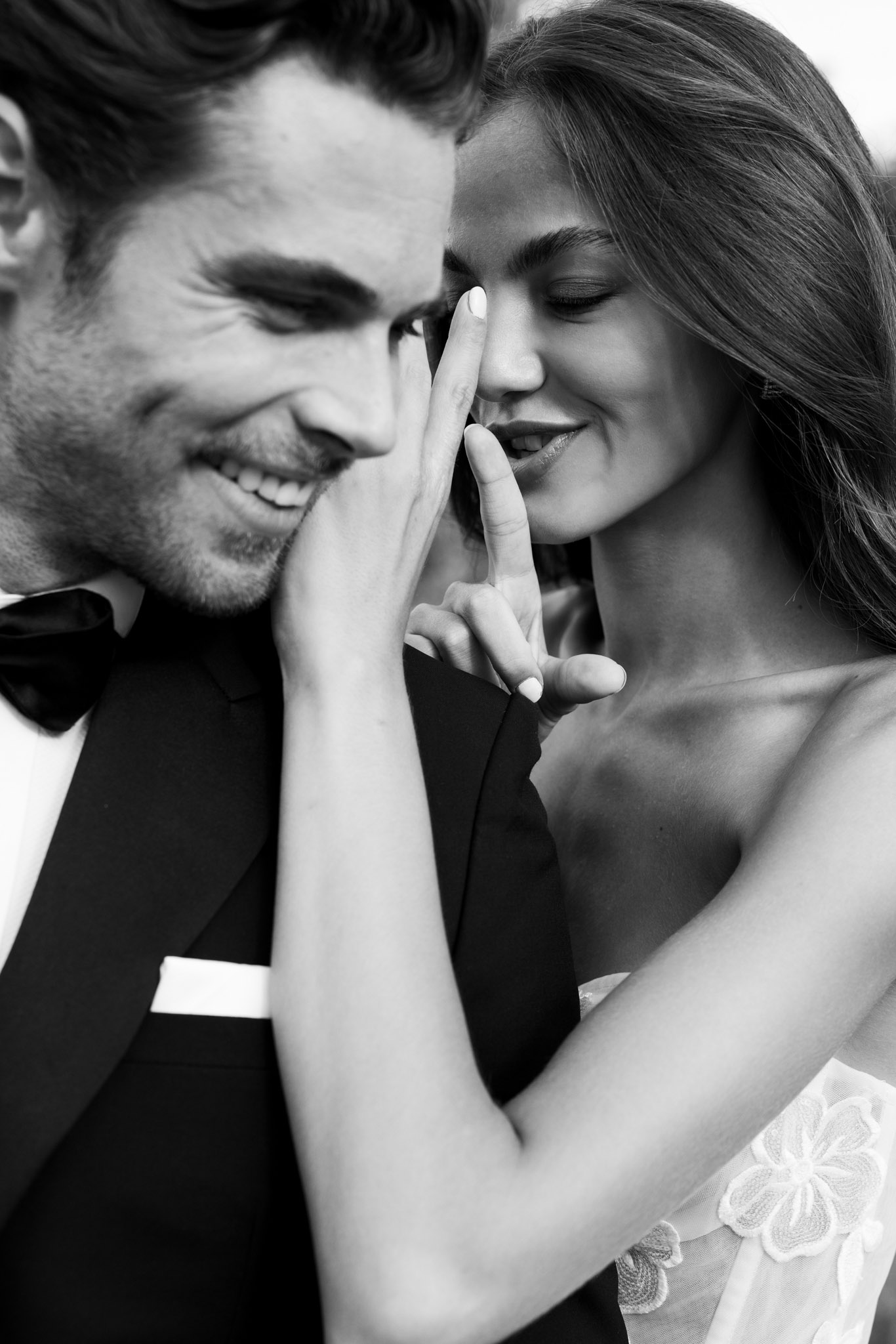 Black and white close-up of bride and groom laughing together, bride touching her face in a playful gesture