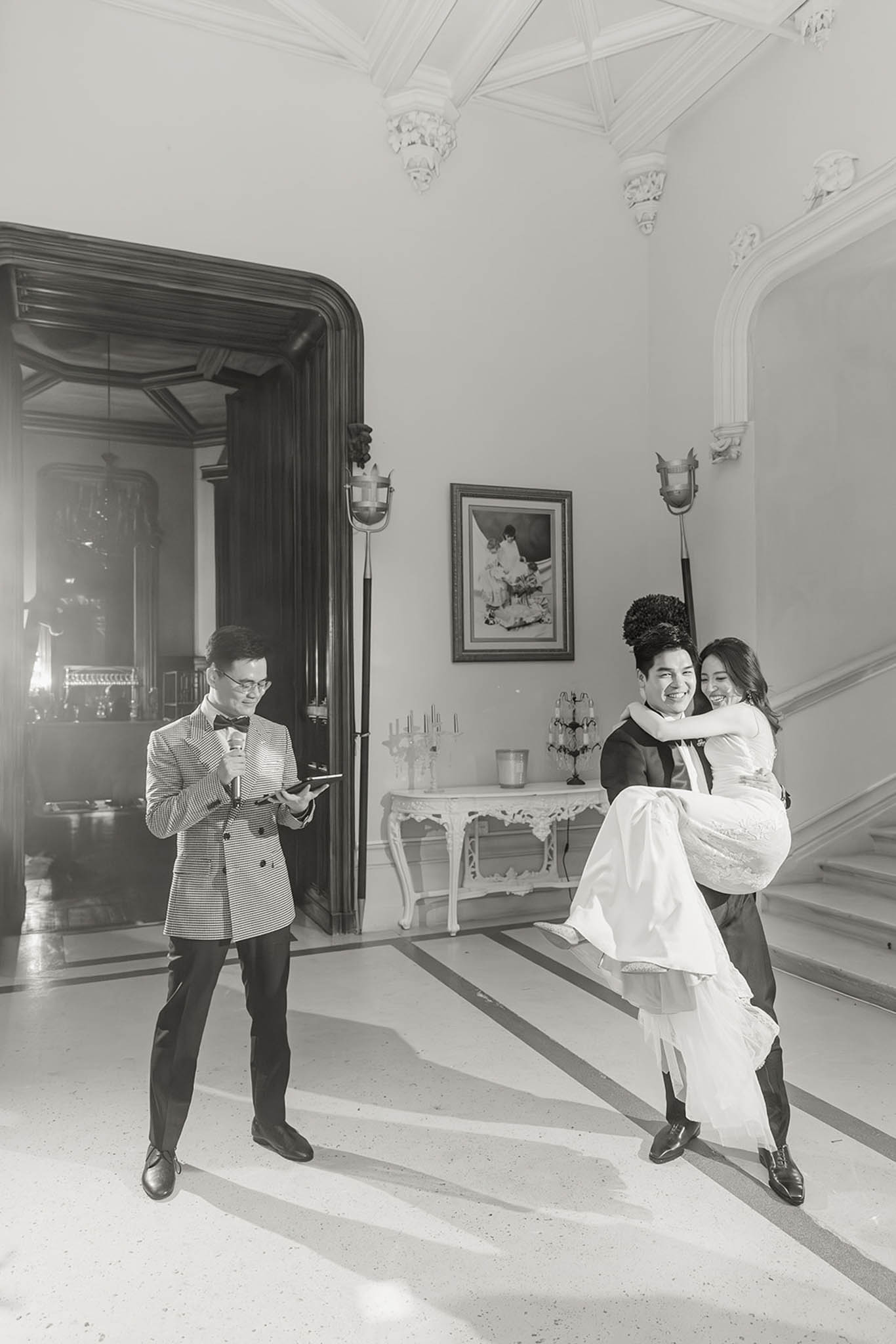 Black and white candid of groom lifting bride in lace gown inside ornate chateau entrance hall