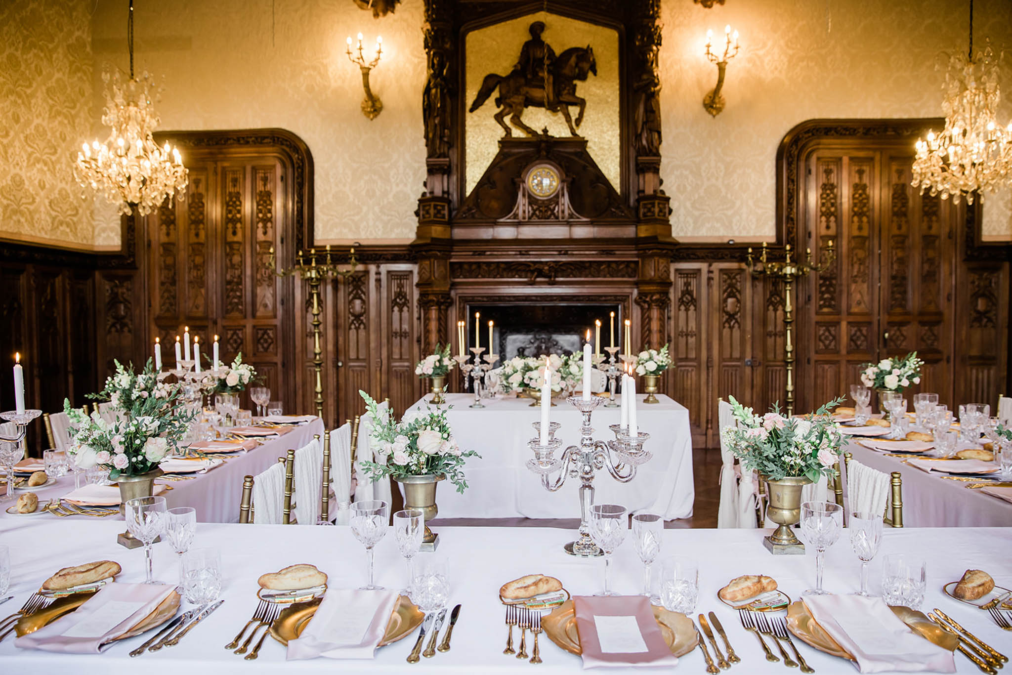 Reception dining room in wood-panelled chateau with long tables set in blush pink and gold with rose centerpieces