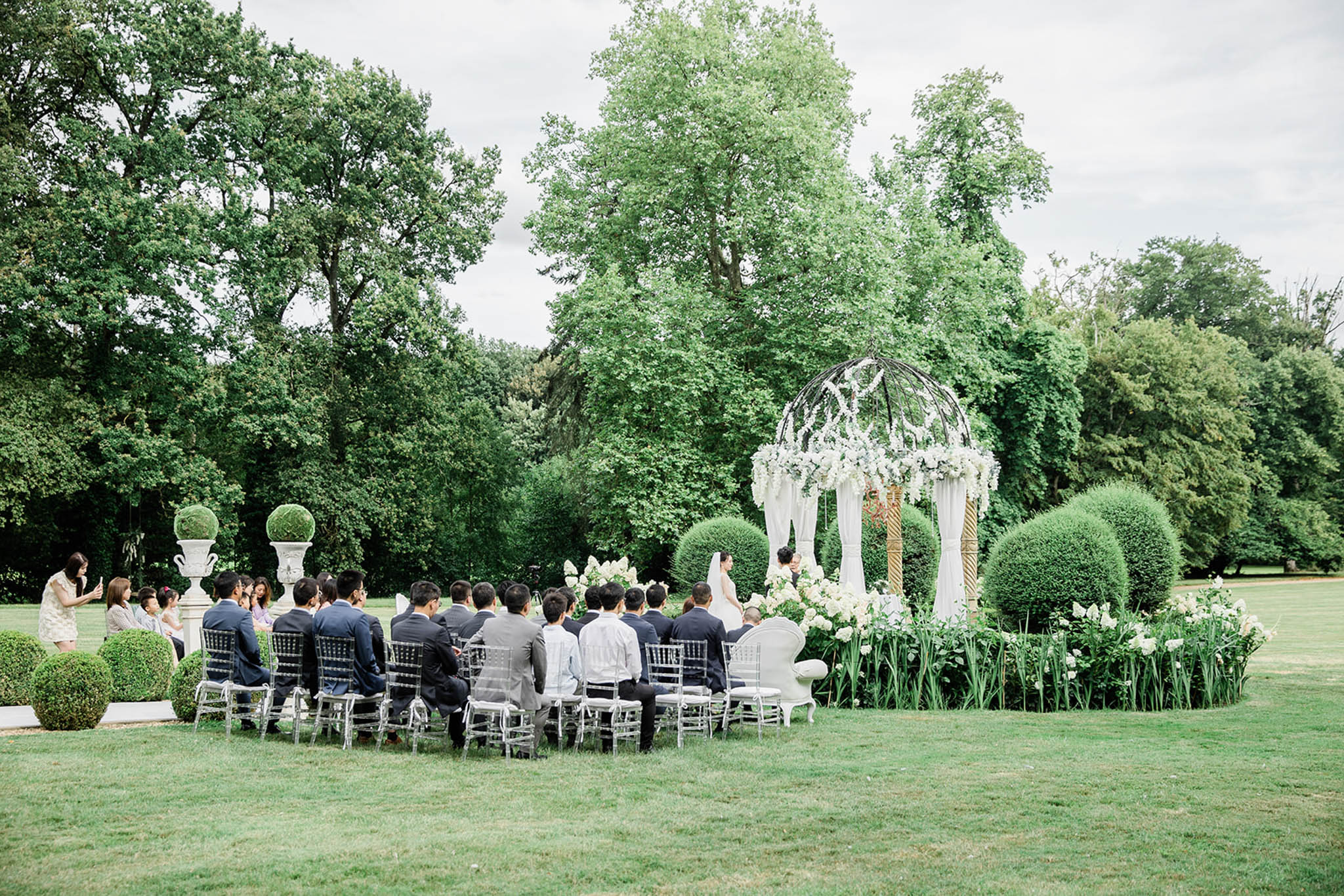 Outdoor ceremony under white-draped gazebo with hydrangea and rose arrangements on formal lawn