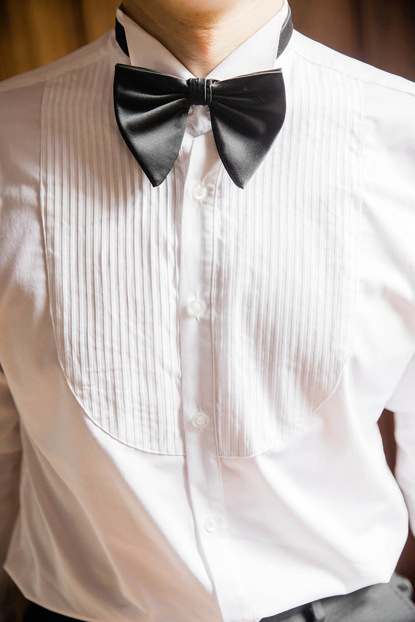 Close-up of groom wearing a white pleated tuxedo shirt with black satin bow tie