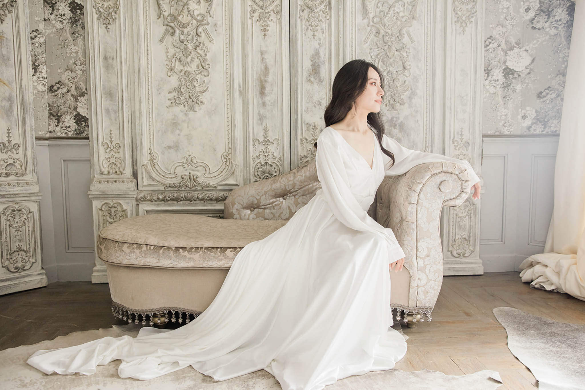 Bride in long-sleeve white gown seated on damask chaise longue in baroque-style French chateau room