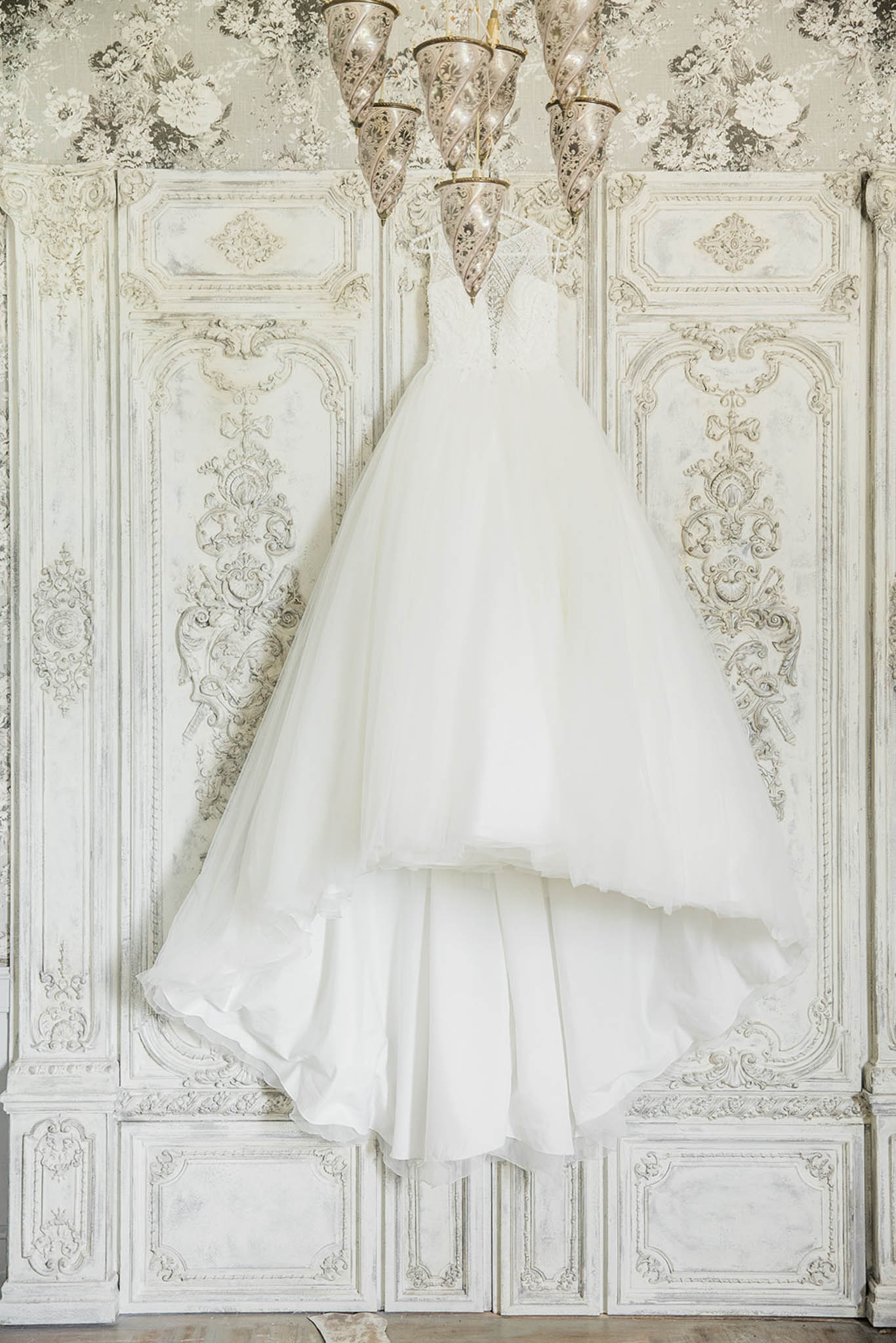 Ivory ballgown with beaded bodice hanging from chandelier against rococo boiserie panels in chateau