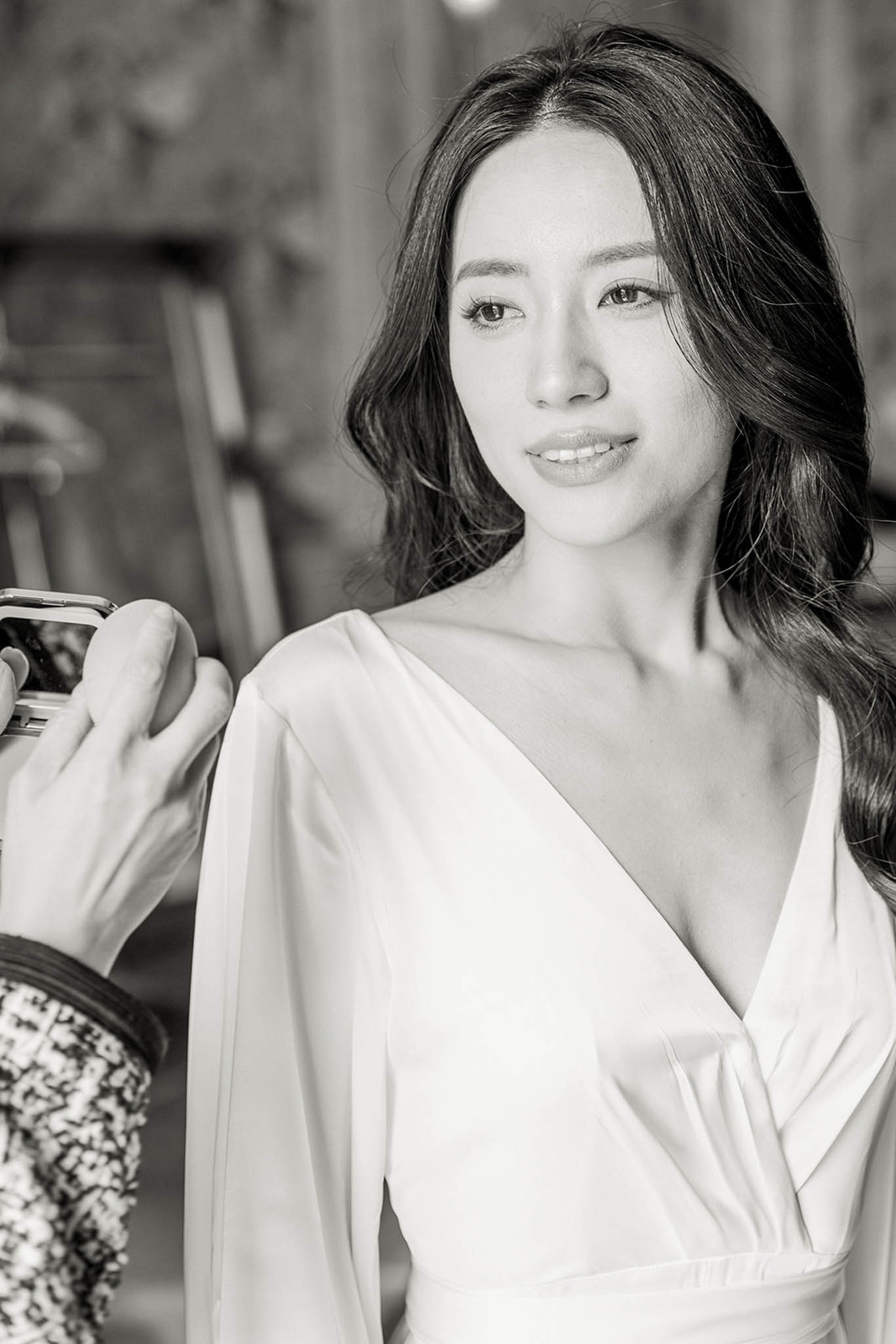 Black and white close-up of bride in white wrap robe during hair and makeup preparation