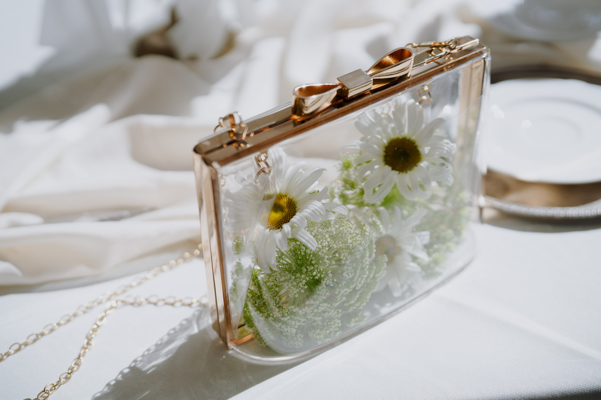 Clear acrylic clutch with rose gold hardware filled with white daisies and Queen Annes lace on white fabric