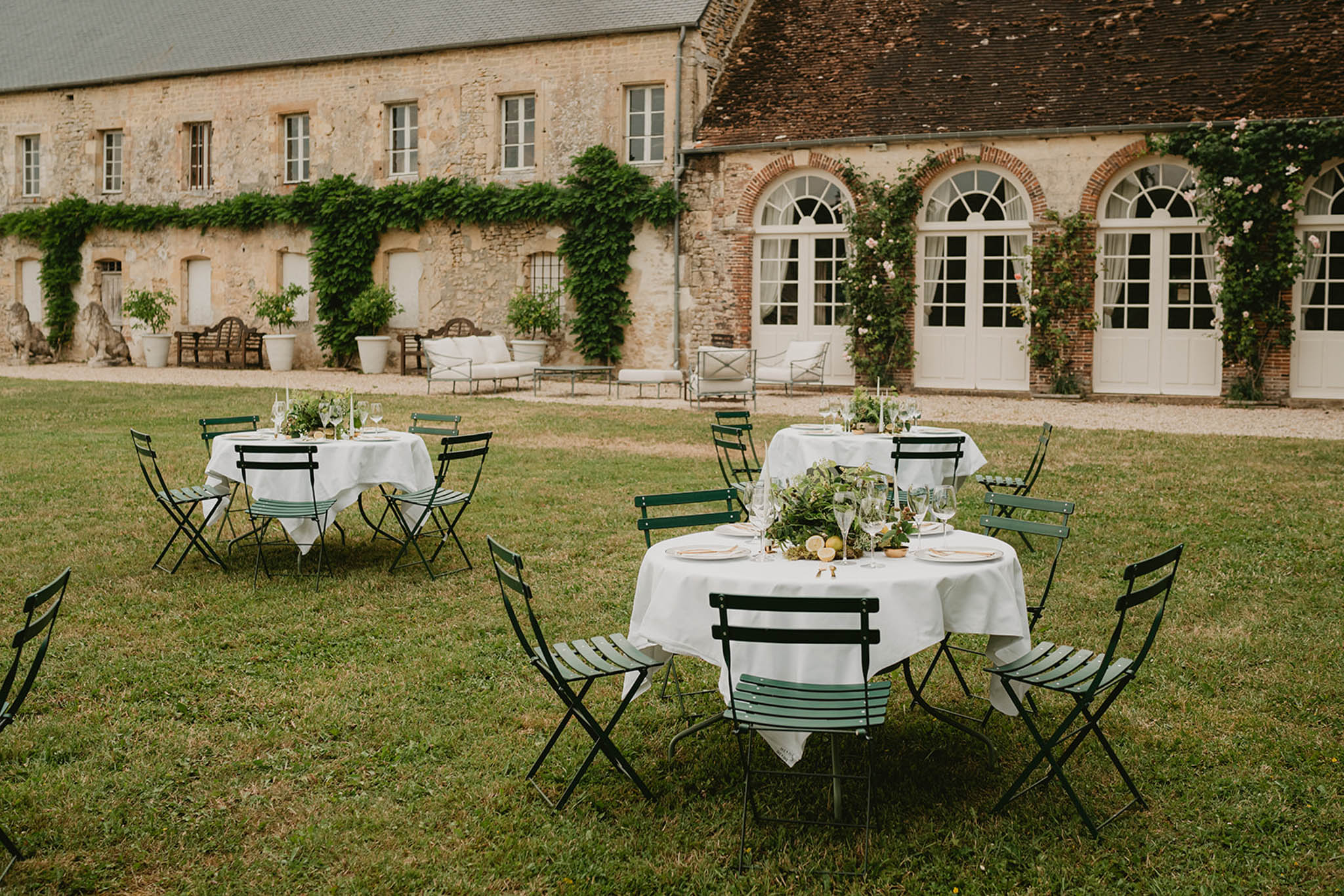 Outdoor reception tables with green bistro chairs and greenery centerpieces on the lawn of a French stone manor