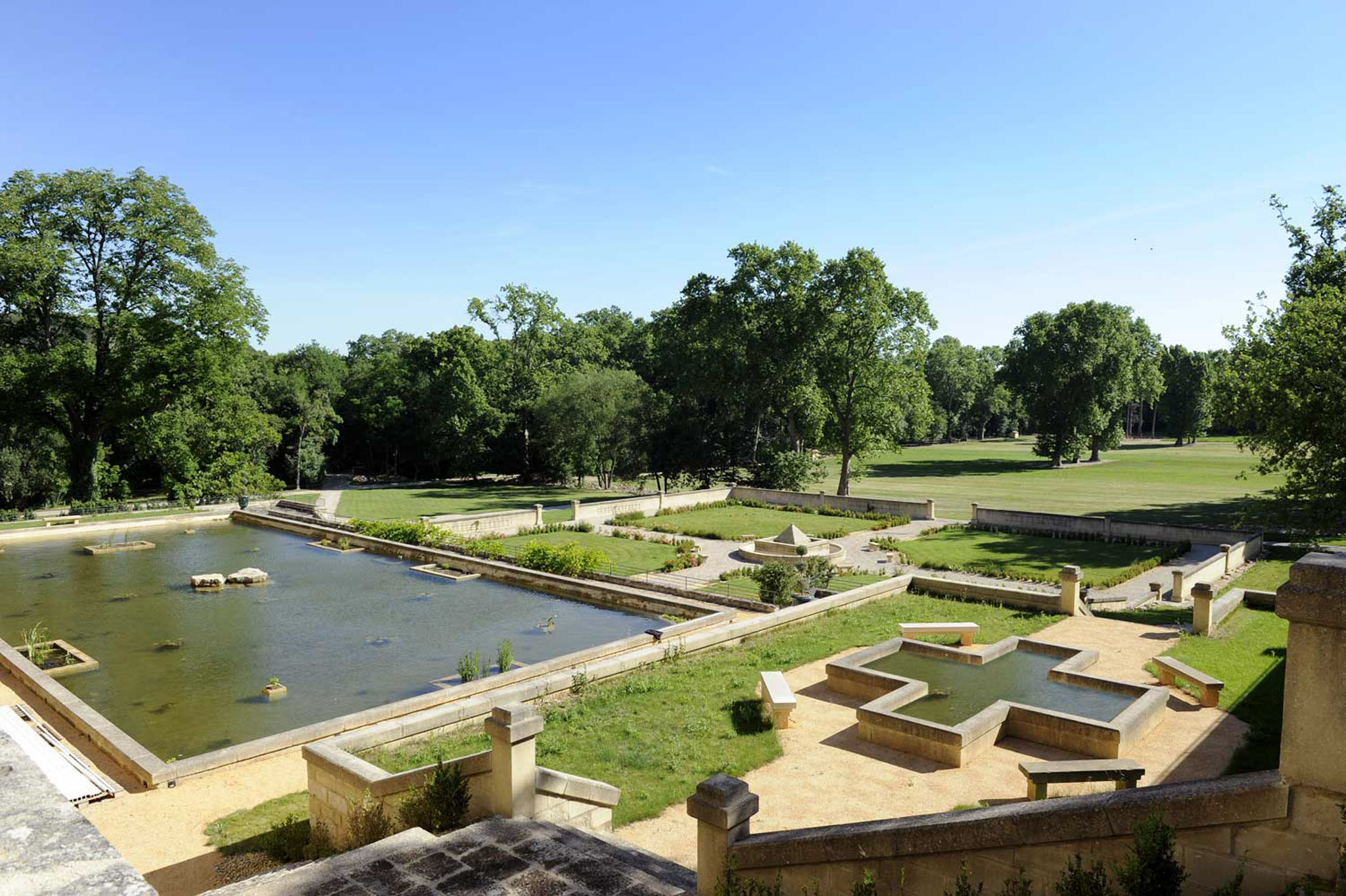 Elevated view of formal chateau grounds with limestone reflecting pool, terraced gardens, and mature trees