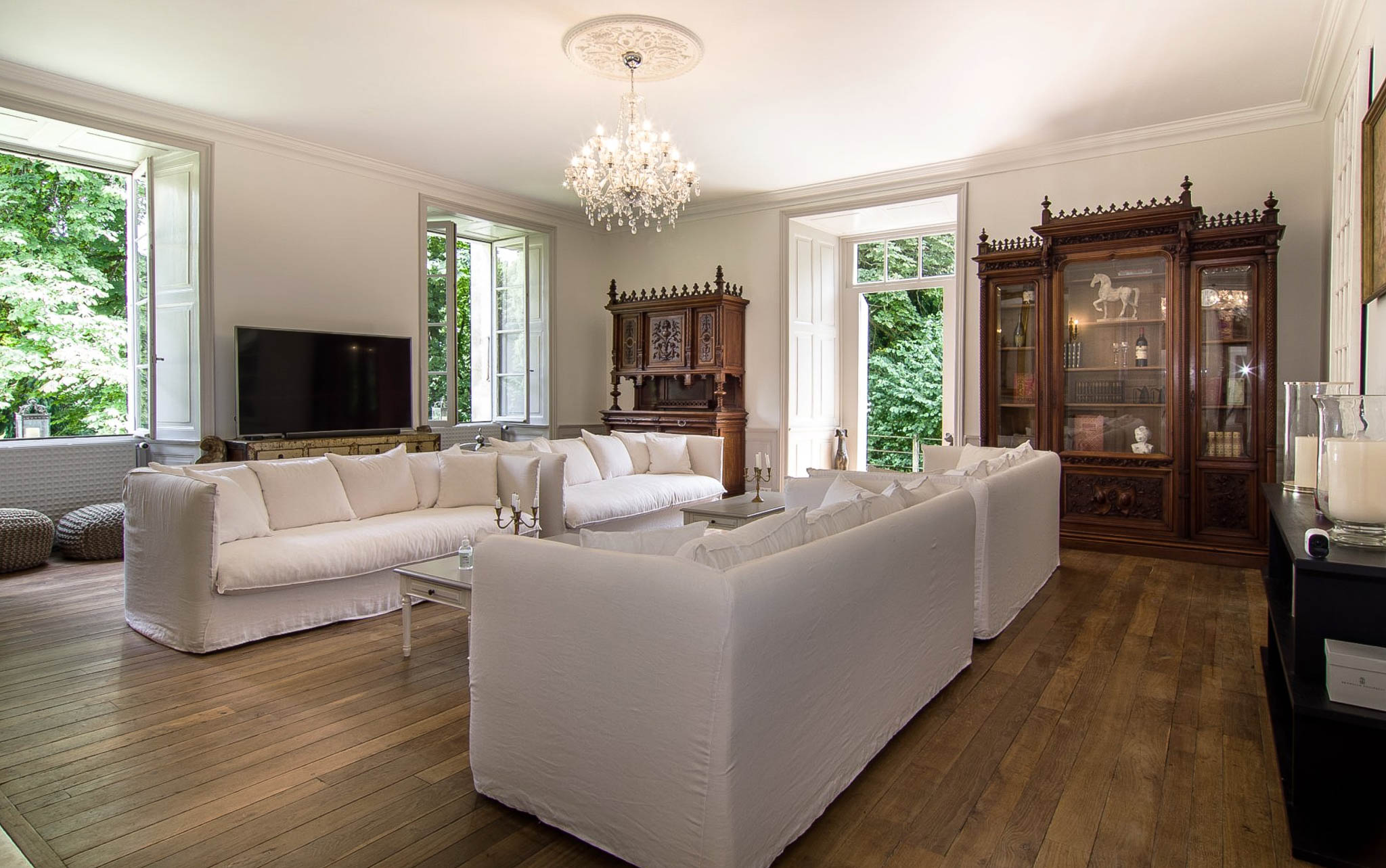White slipcovered sofas with crystal chandelier and carved walnut antique cabinets in chateau reception room