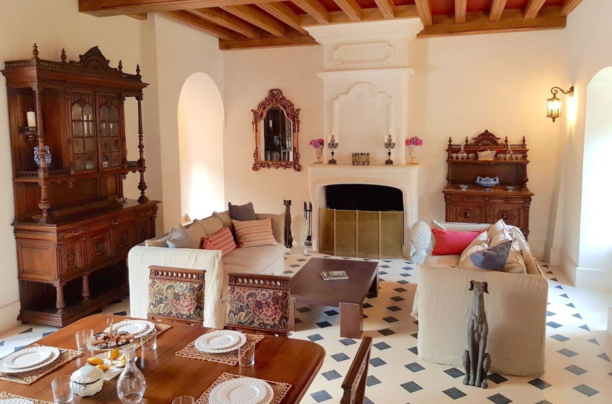 Grand chateau salon with exposed beam ceiling, antique armoires, stone fireplace, and diamond-pattern tile floor