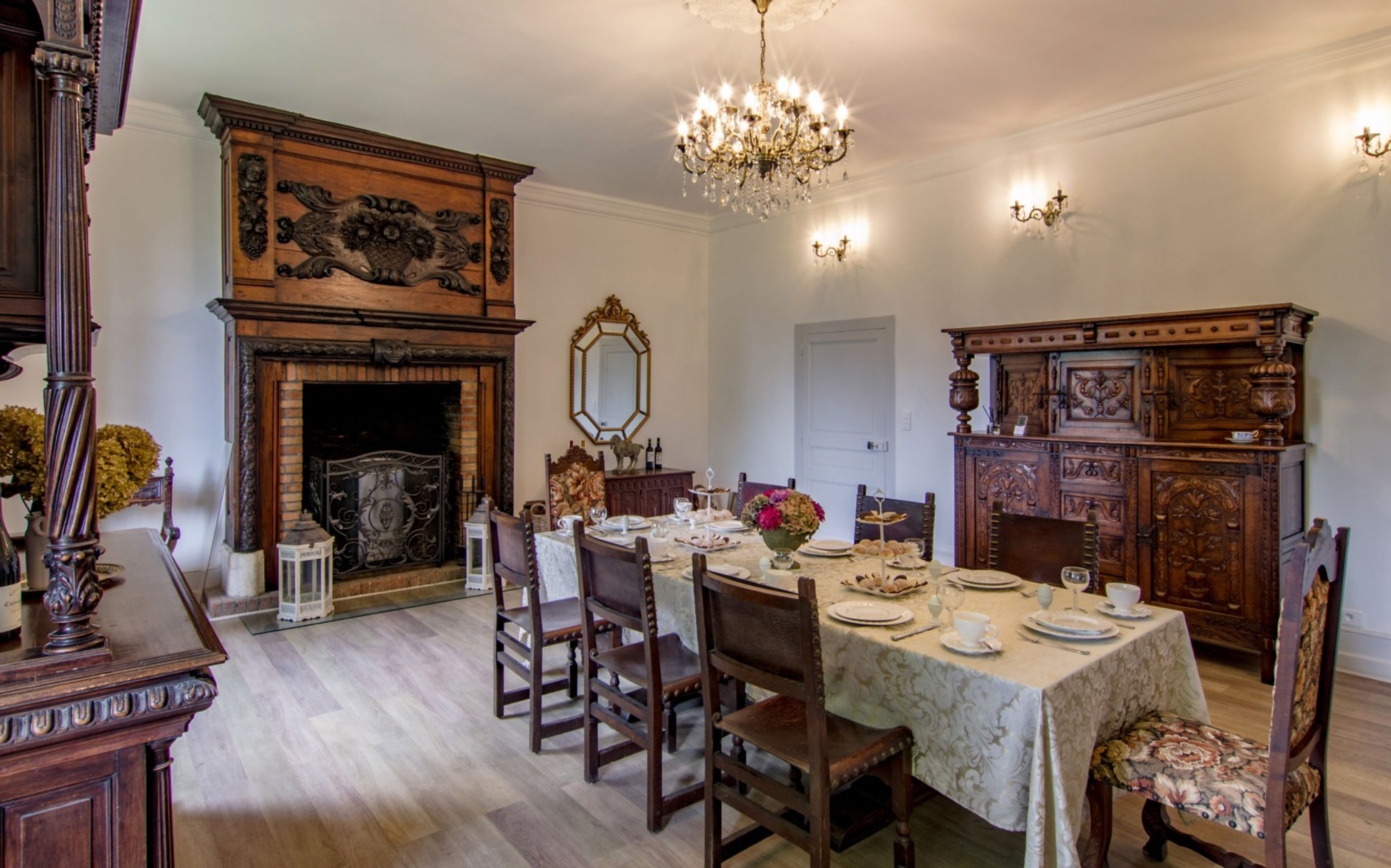 Formal dining room in French chateau with carved fireplace, crystal chandelier, and pink hydrangea centerpiece