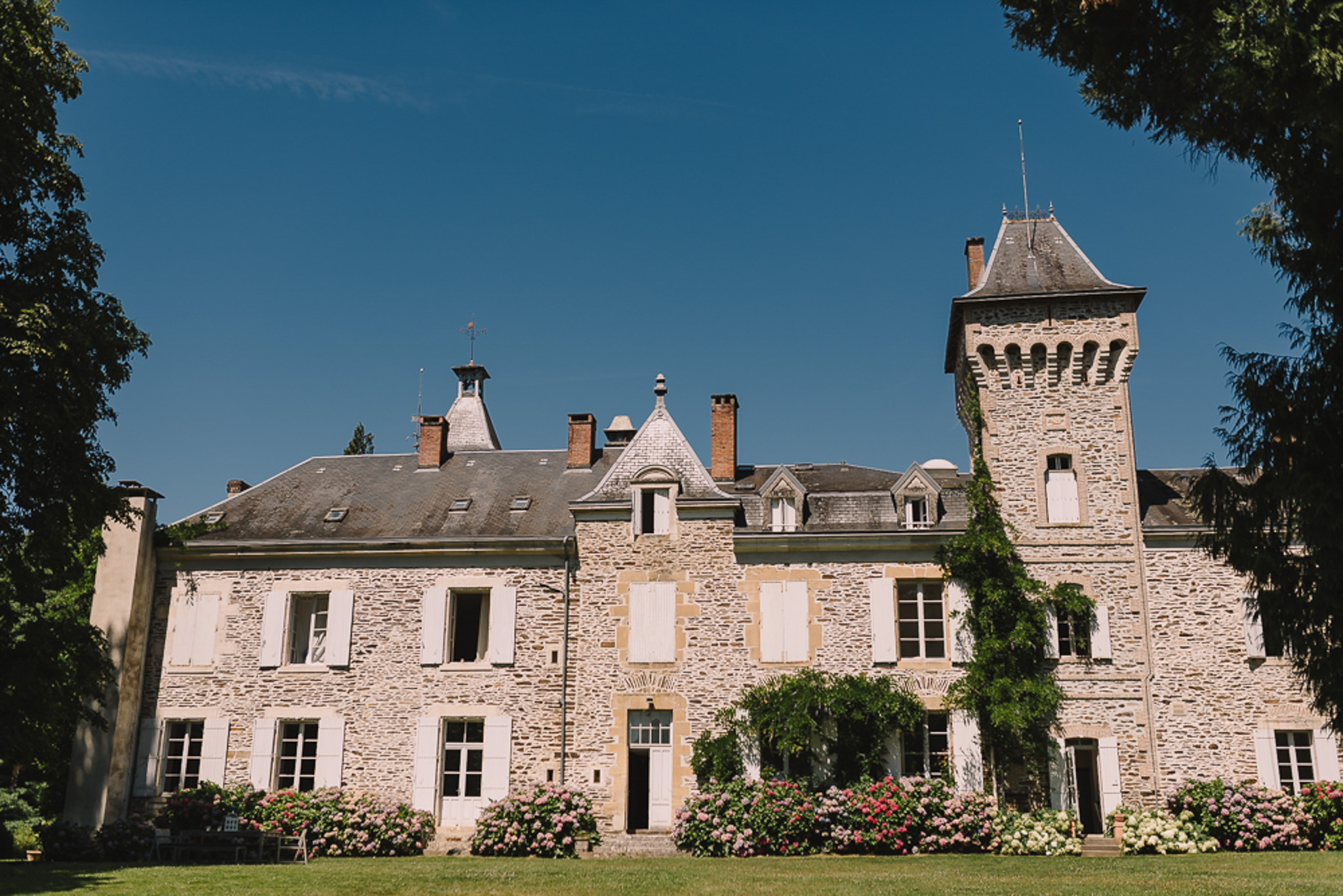 Stone chateau with mansard roof, square tower, and pink hydrangea border