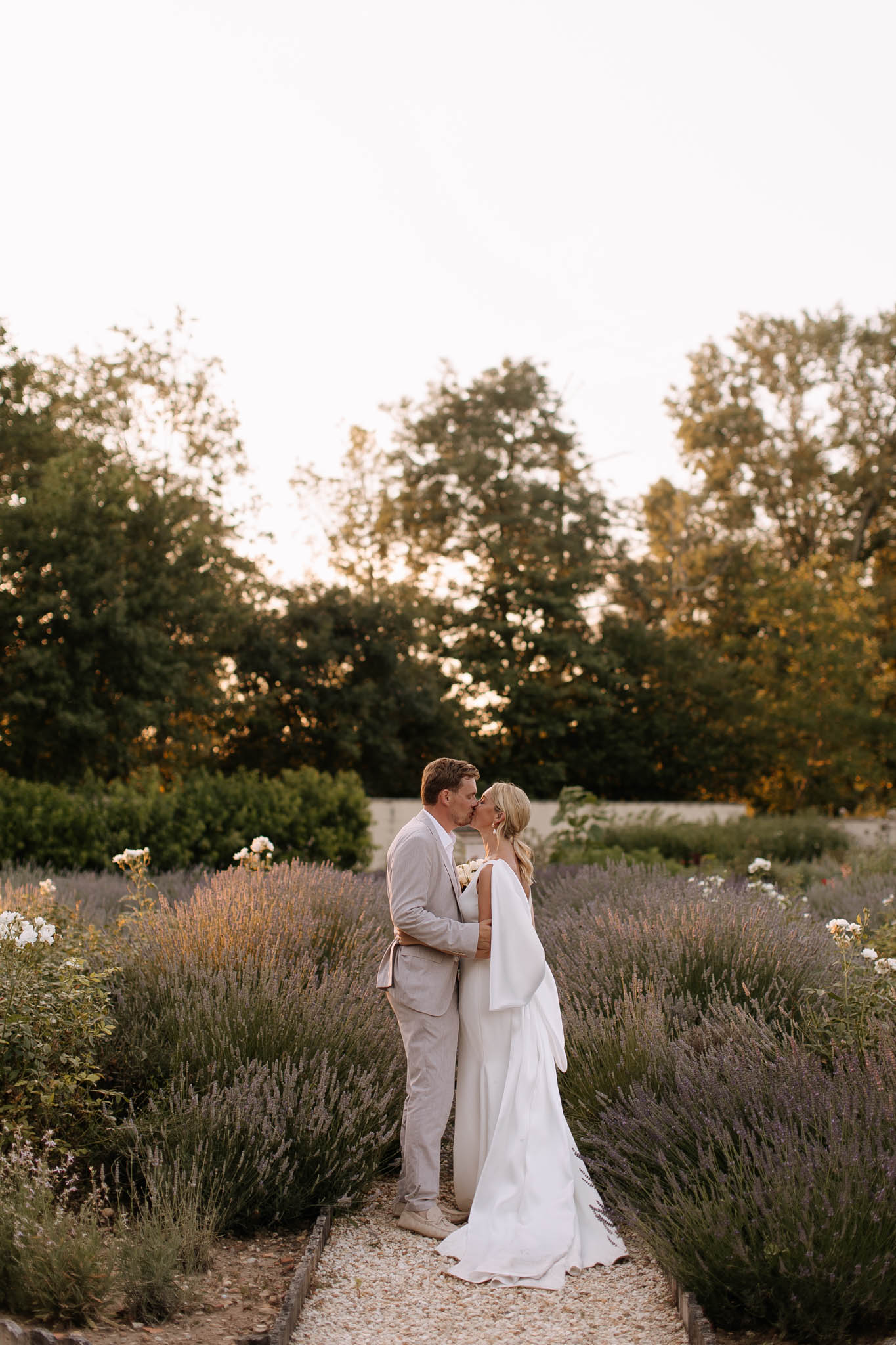 Couple kissing on gravel path through lavender and rose garden at golden hour