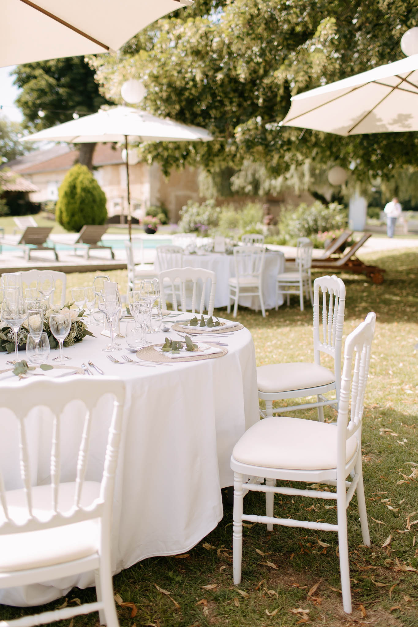 Garden reception with round tables under market umbrellas, white floral centerpieces, and eucalyptus place settings